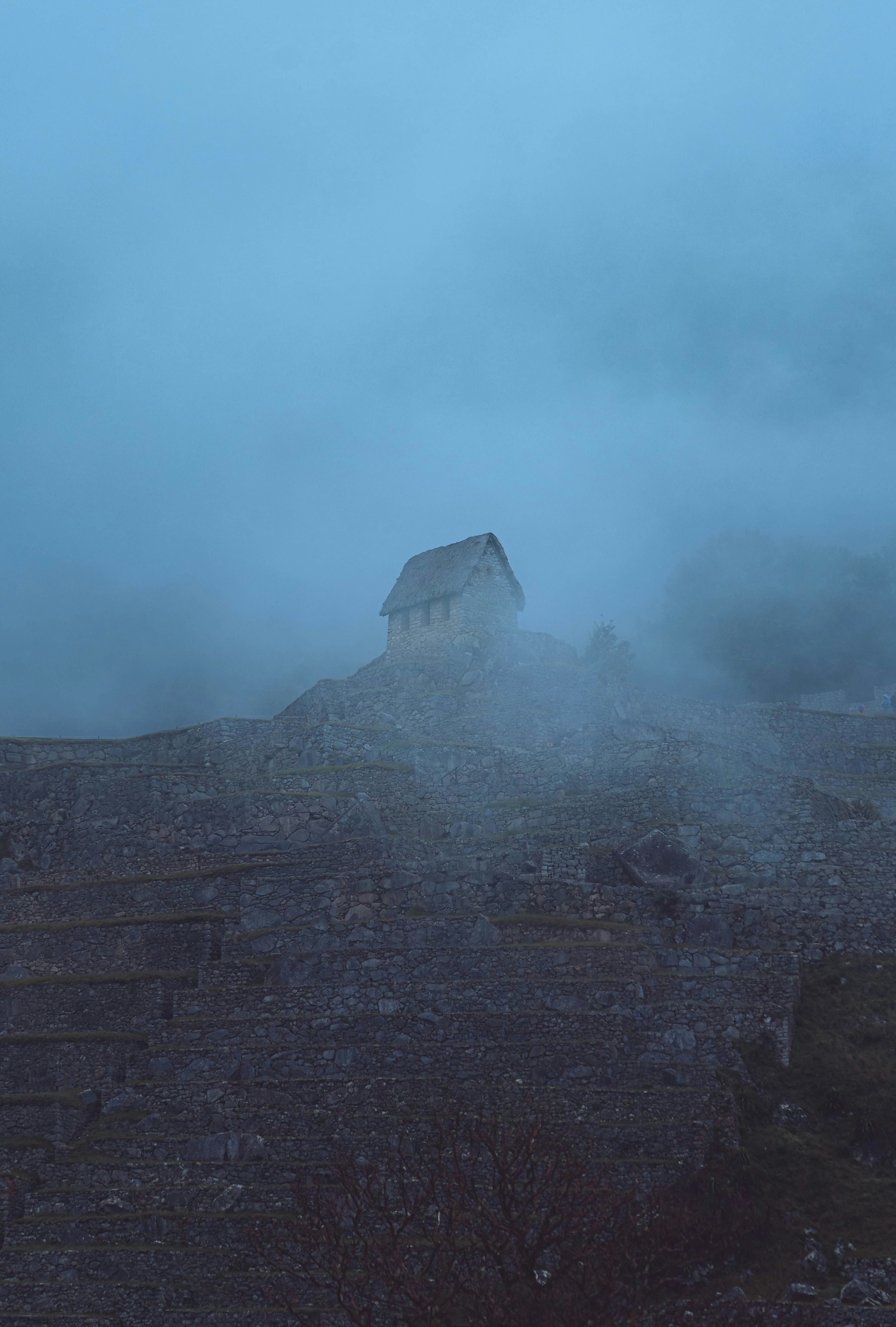 Kleine Steinhütte auf einem felsigen Hügel im Nebel.