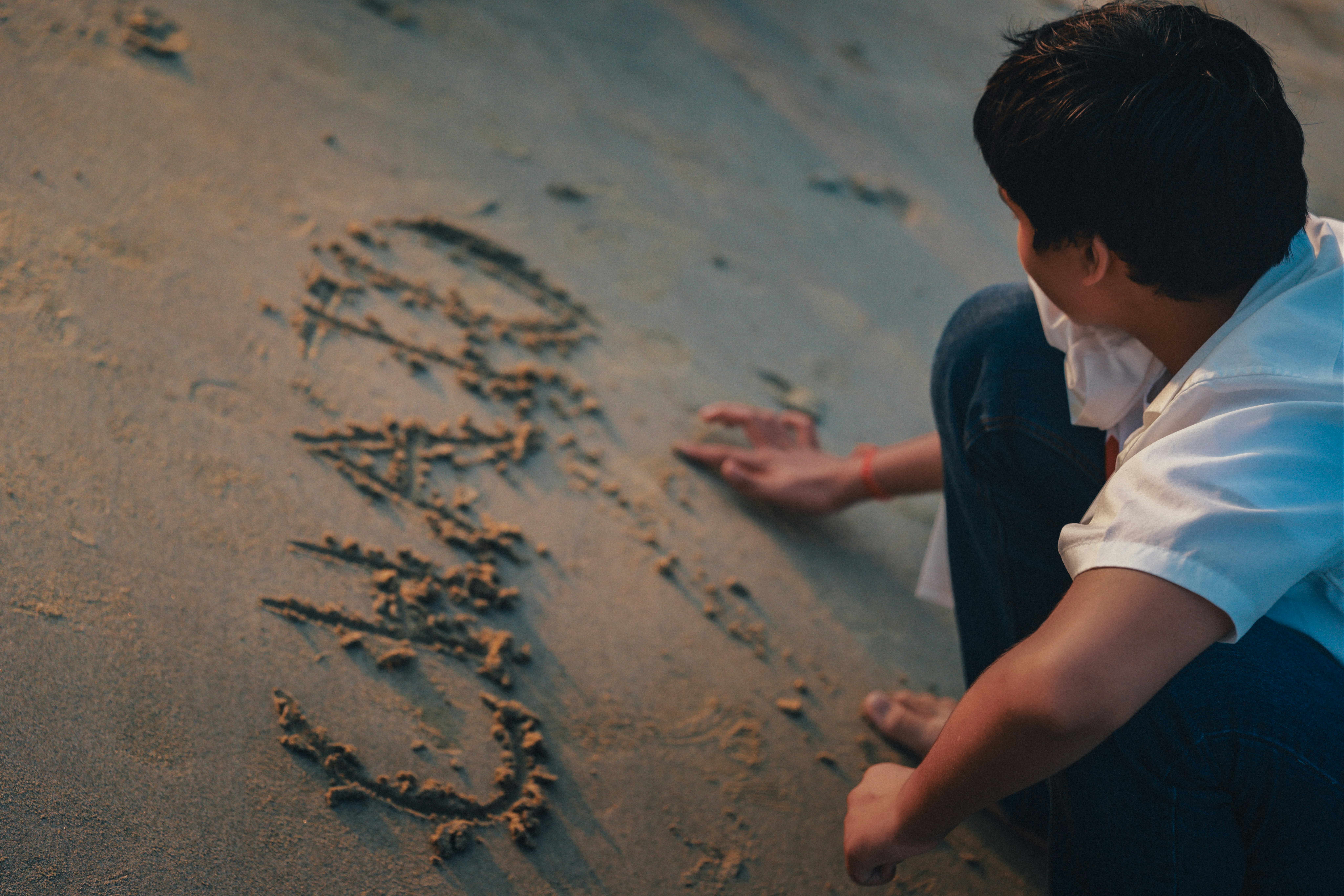 A person writing on a sandy beach.