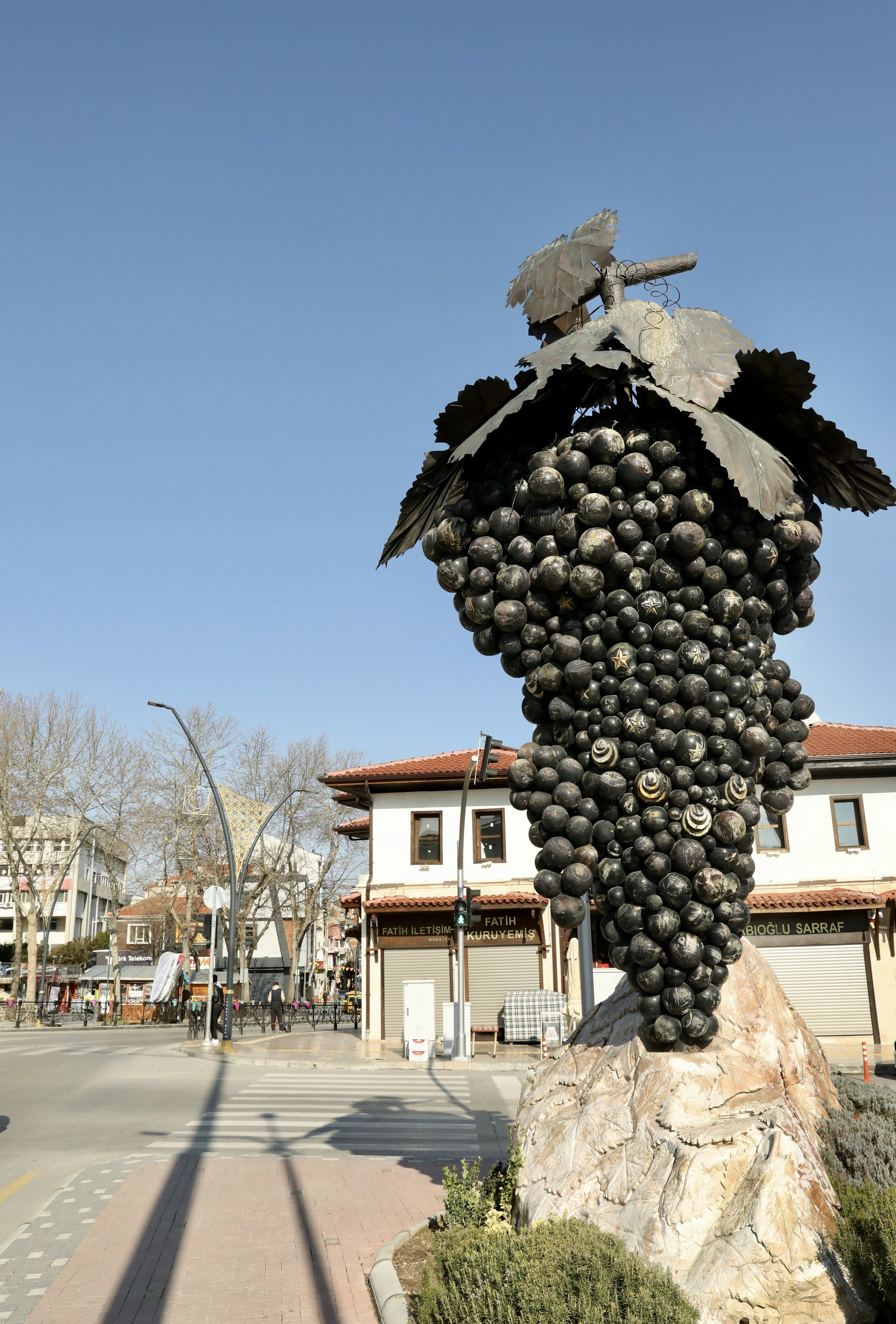 Large grape sculpture on a stone base outdoors.