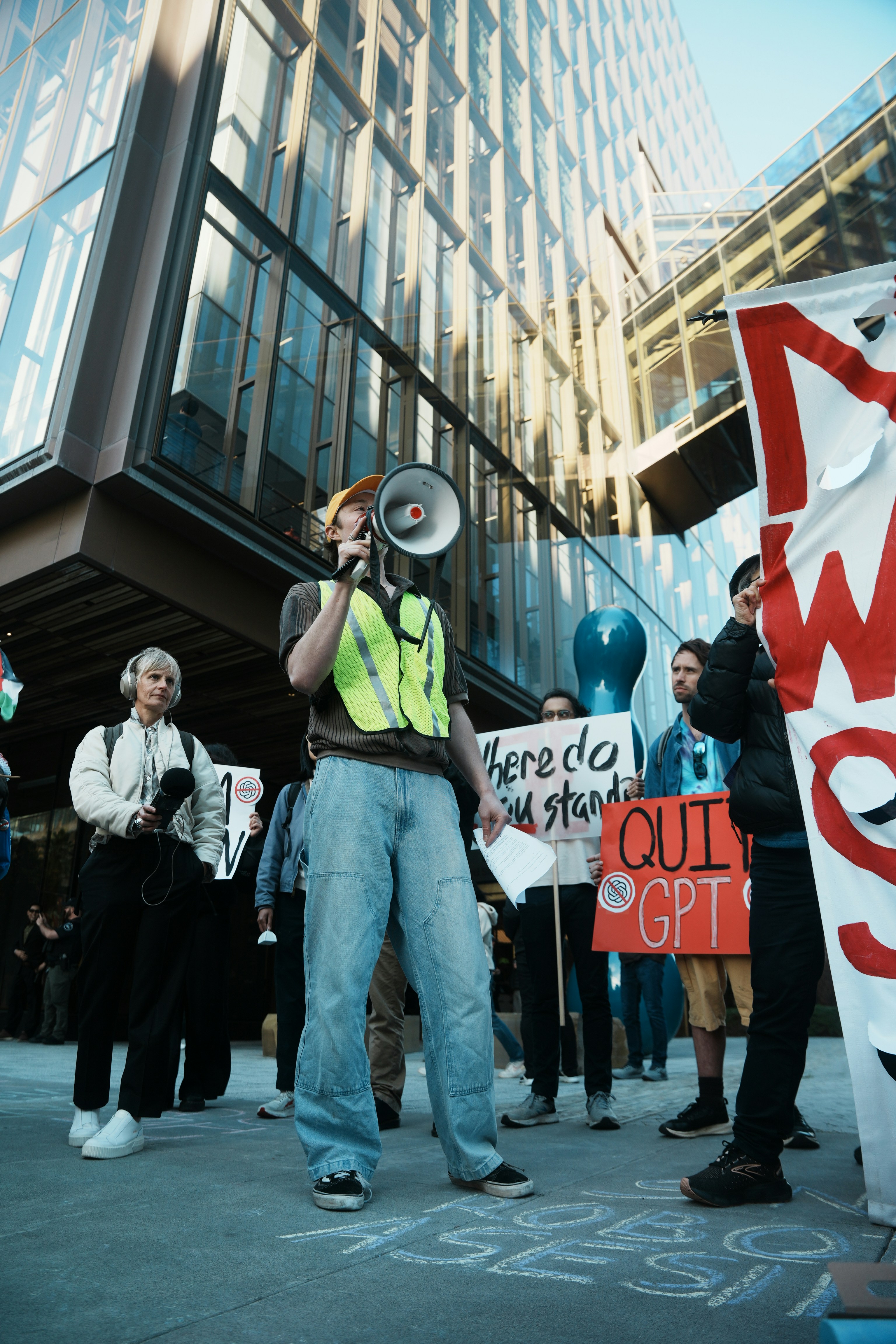 Protesters with signs and megaphones outside modern building.