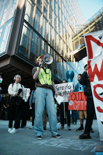 Protesters with signs and megaphones outside modern building.