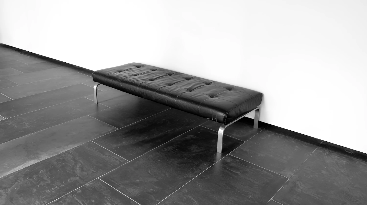 A black buttoned waiting bench against a white wall on a dark tiled floor