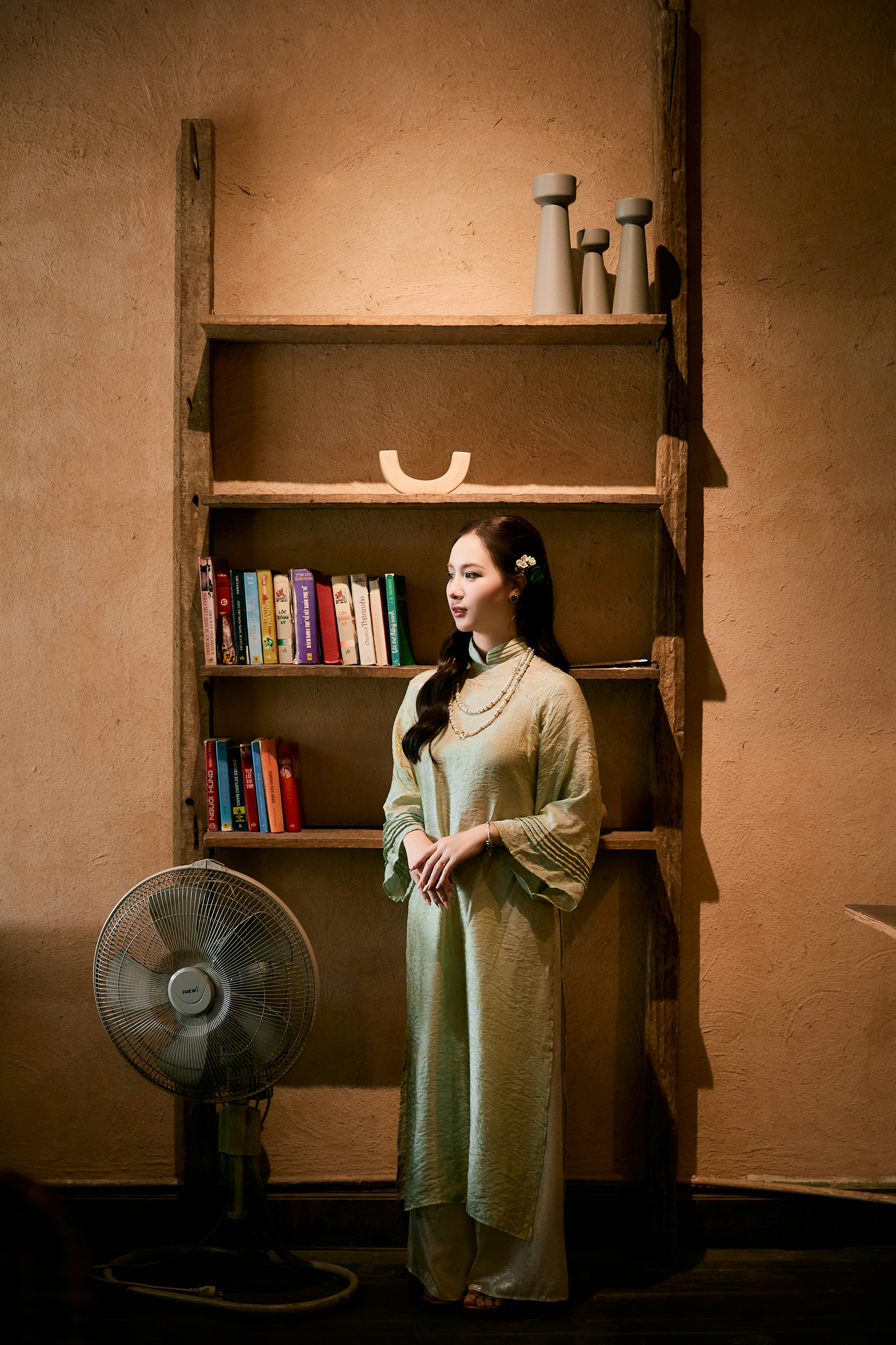 A woman in a traditional dress stands by a bookshelf.