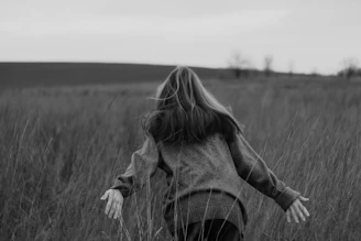 A person with long hair runs through a grassy field.