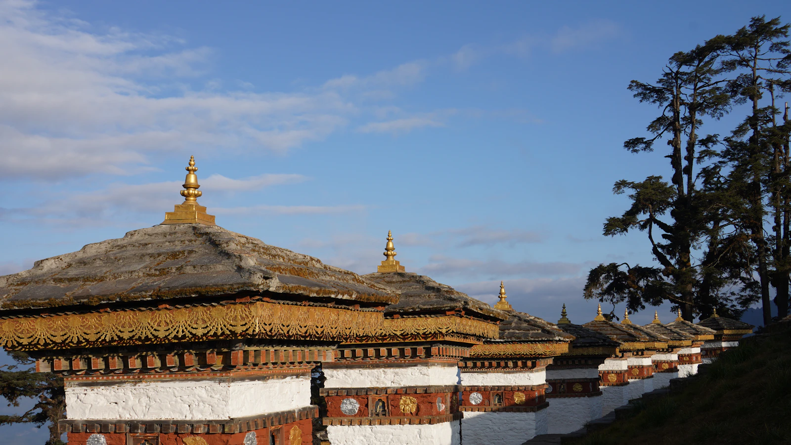 The Druk Wangyal chortens at Dochu La in low golden light, their gilded finials against a pale blue sky