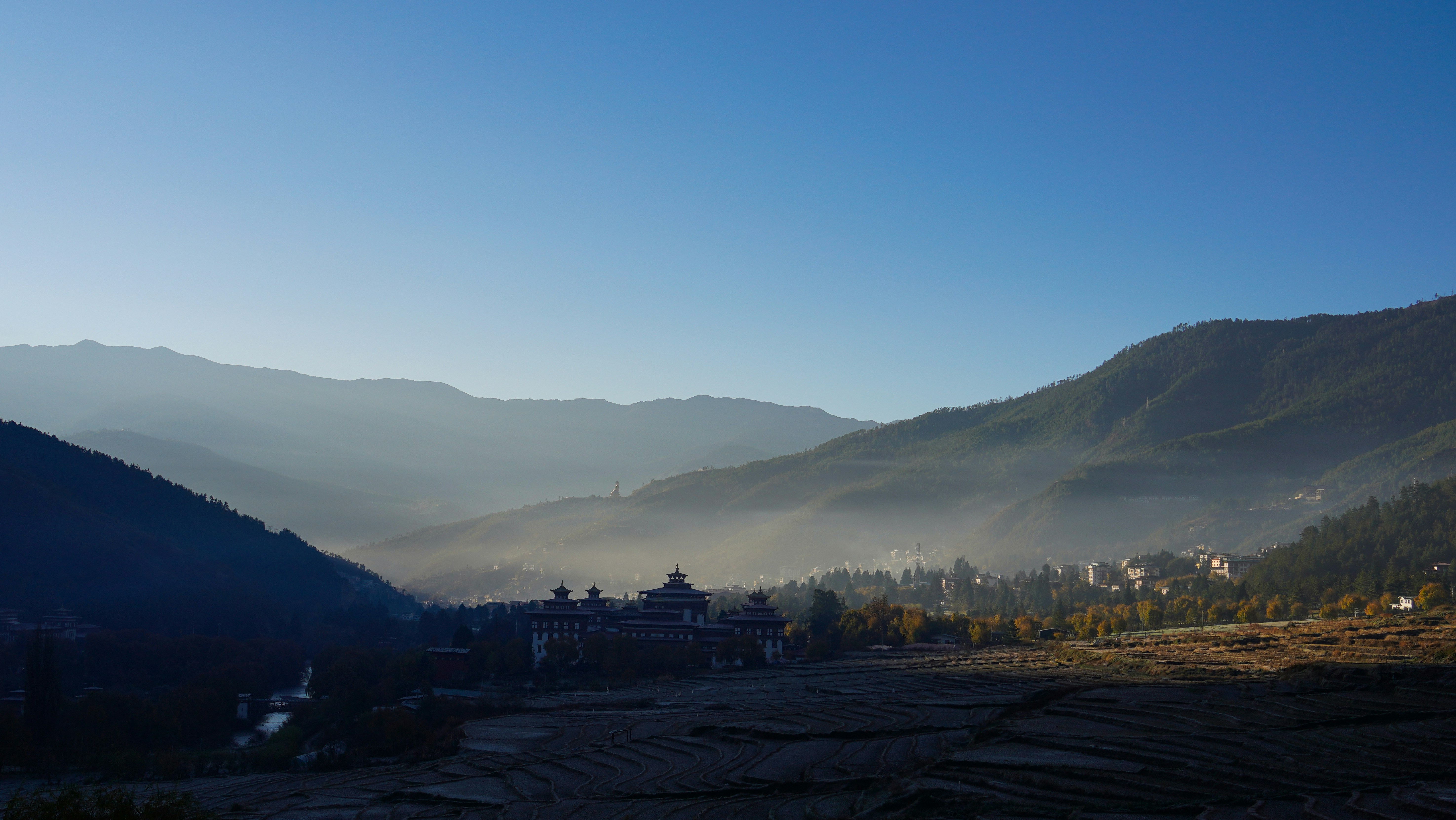 Valle montañoso brumoso con edificios al amanecer