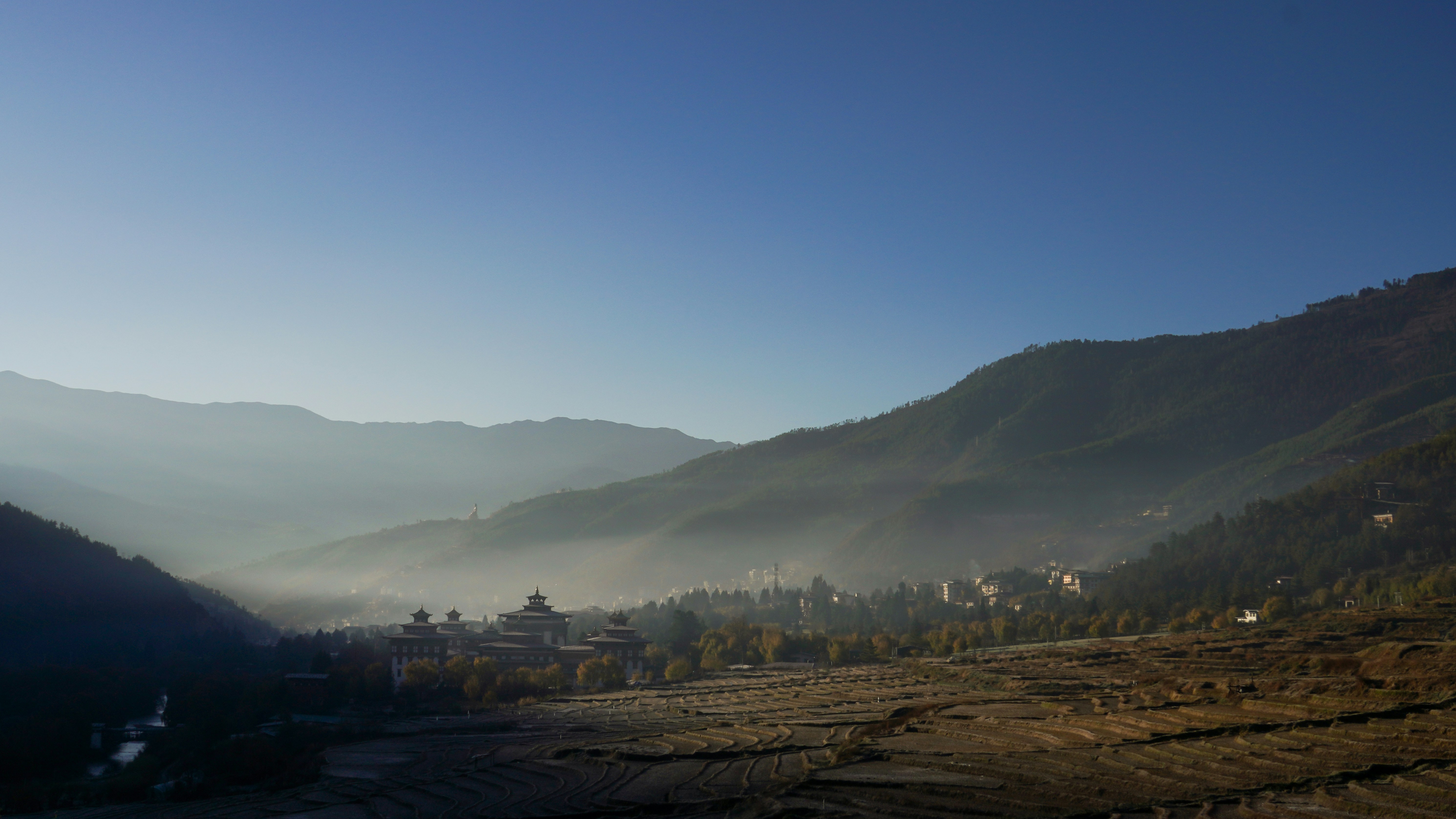 Valle brumoso con montañas y un cielo azul despejado.
