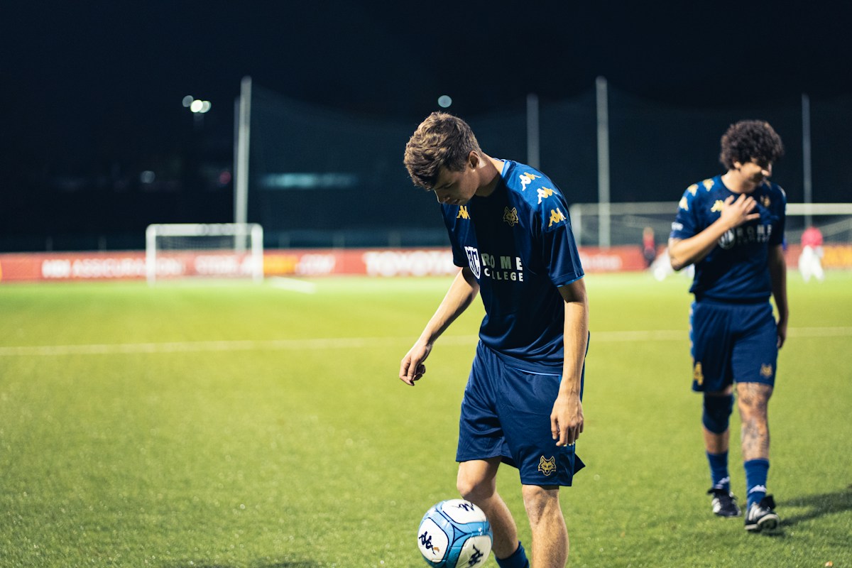 Two young men in soccer uniforms on a field, representing youth sports teamwork and coordination.