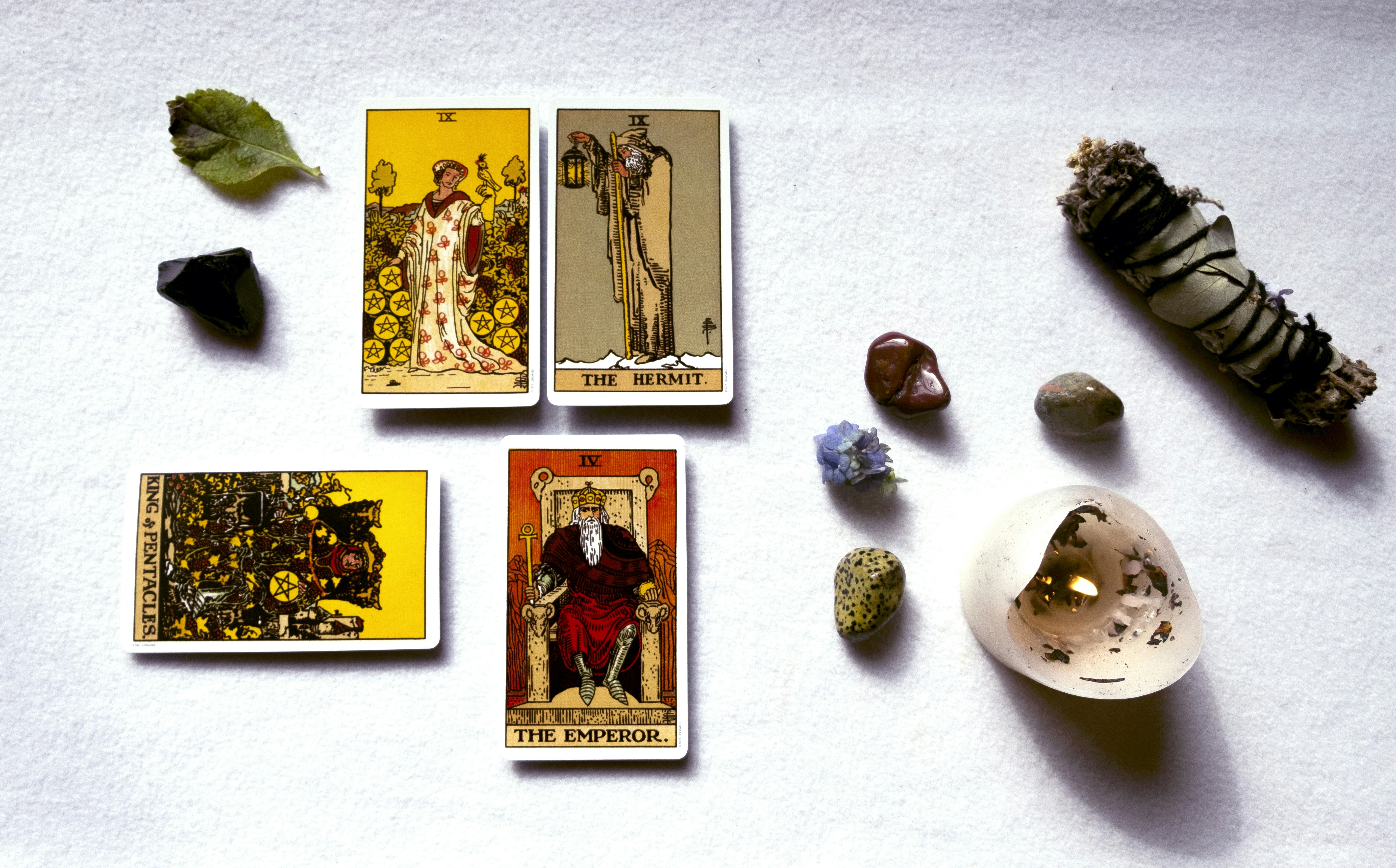 Cartas de tarô, cristais e sálvia sobre superfície branca.