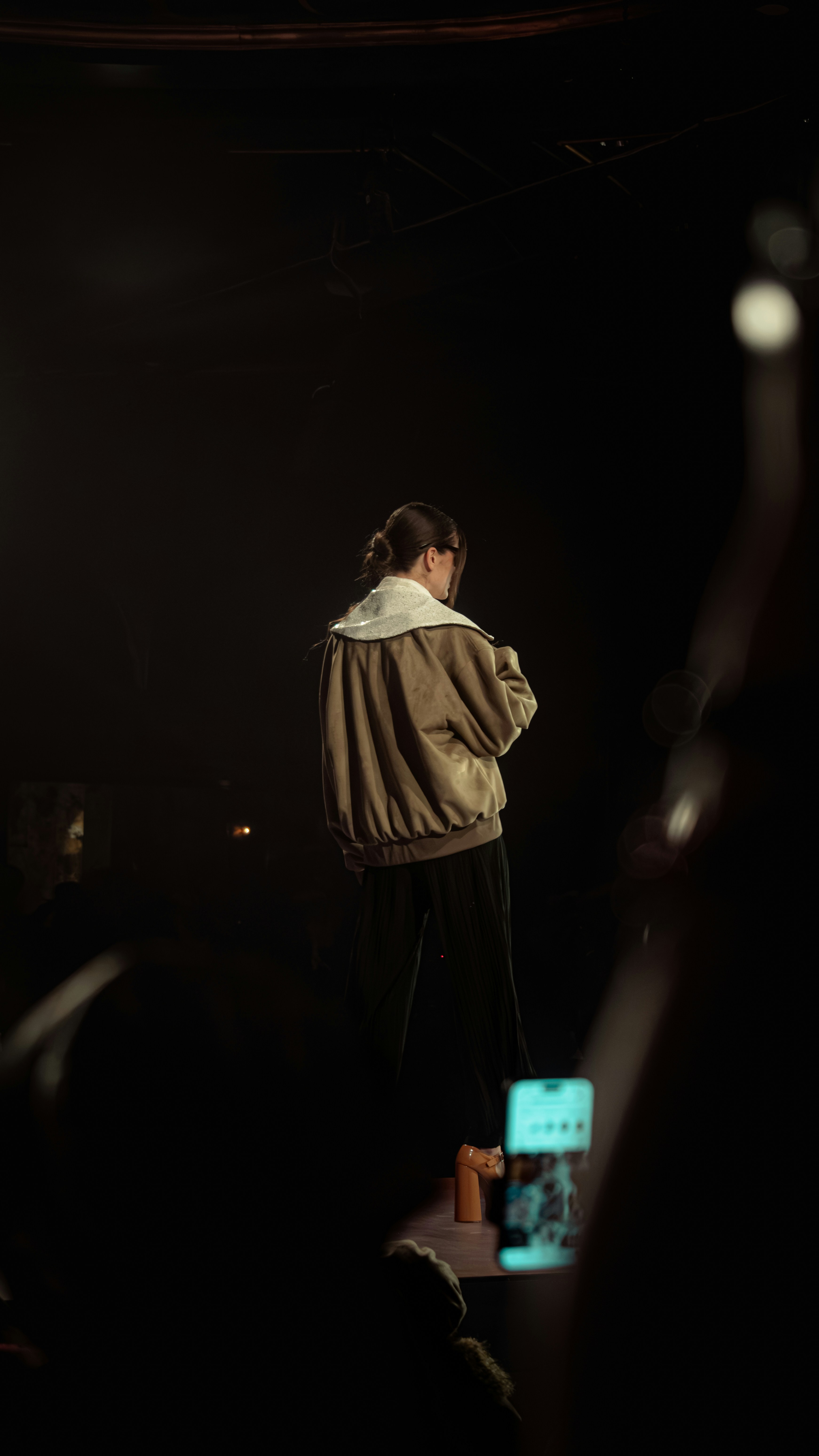 Mujer con chaqueta bomber en un escenario tenuemente iluminado