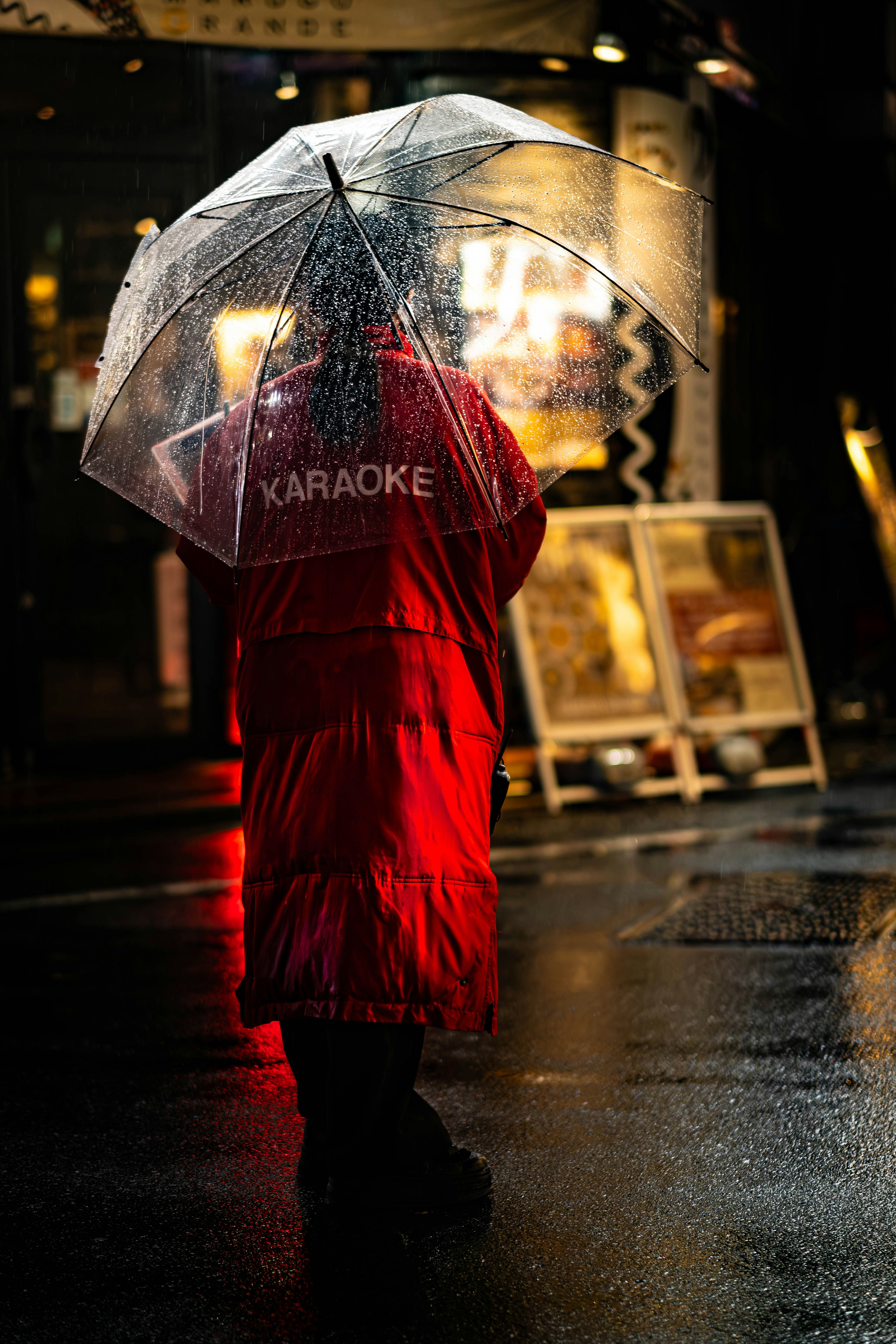 Person in red coat holding umbrella on rainy night