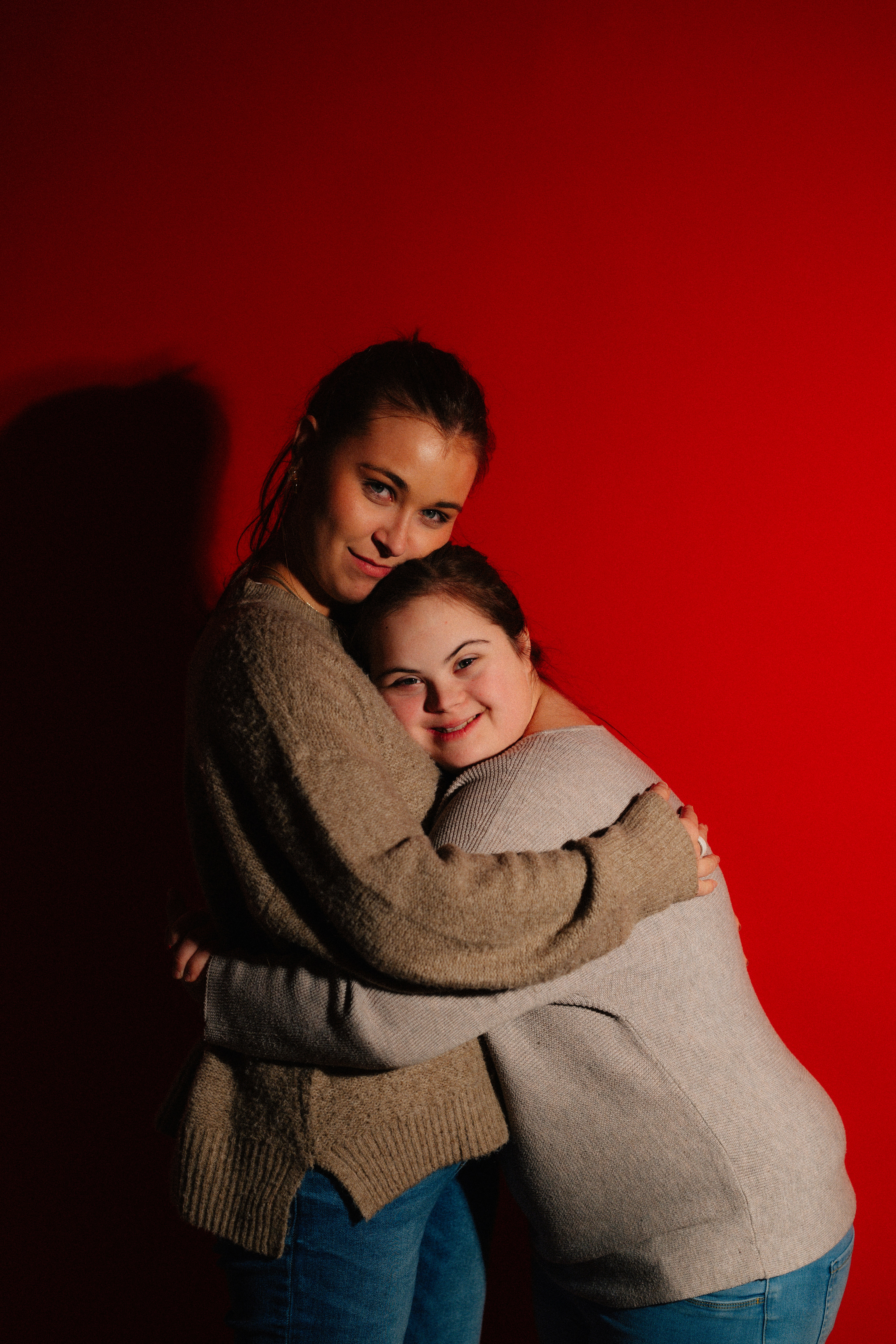 Two women hugging against a red background.