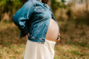 Pregnant woman in denim jacket and white skirt outdoors