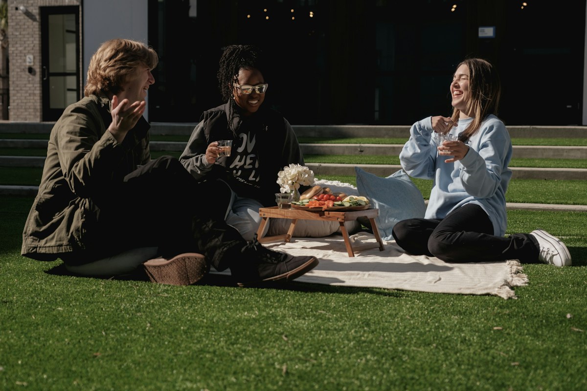Three friends having a picnic on the grass, ideal for summer camp activities and bonding experiences.