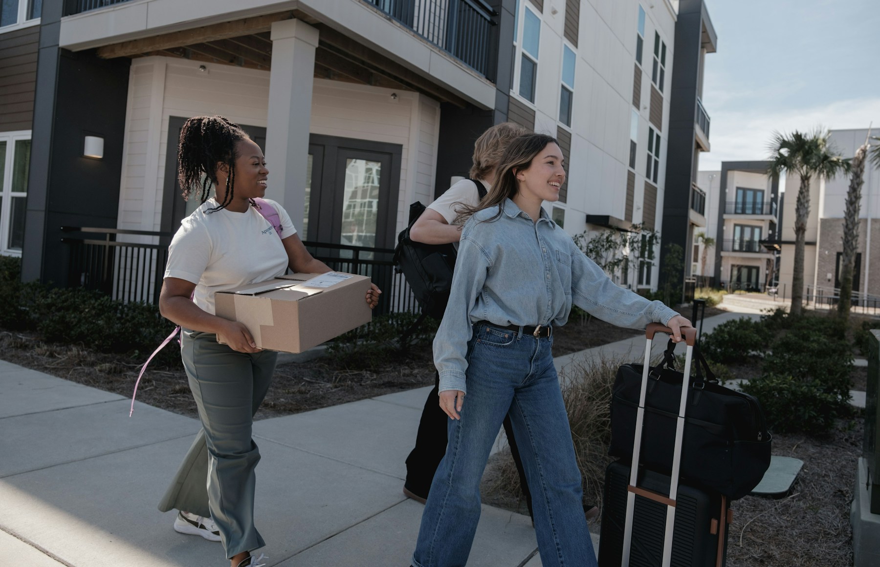 Young people carrying moving boxes and luggage into a building during college move-in day