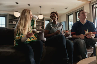 Friends laughing while watching a sports game at home.