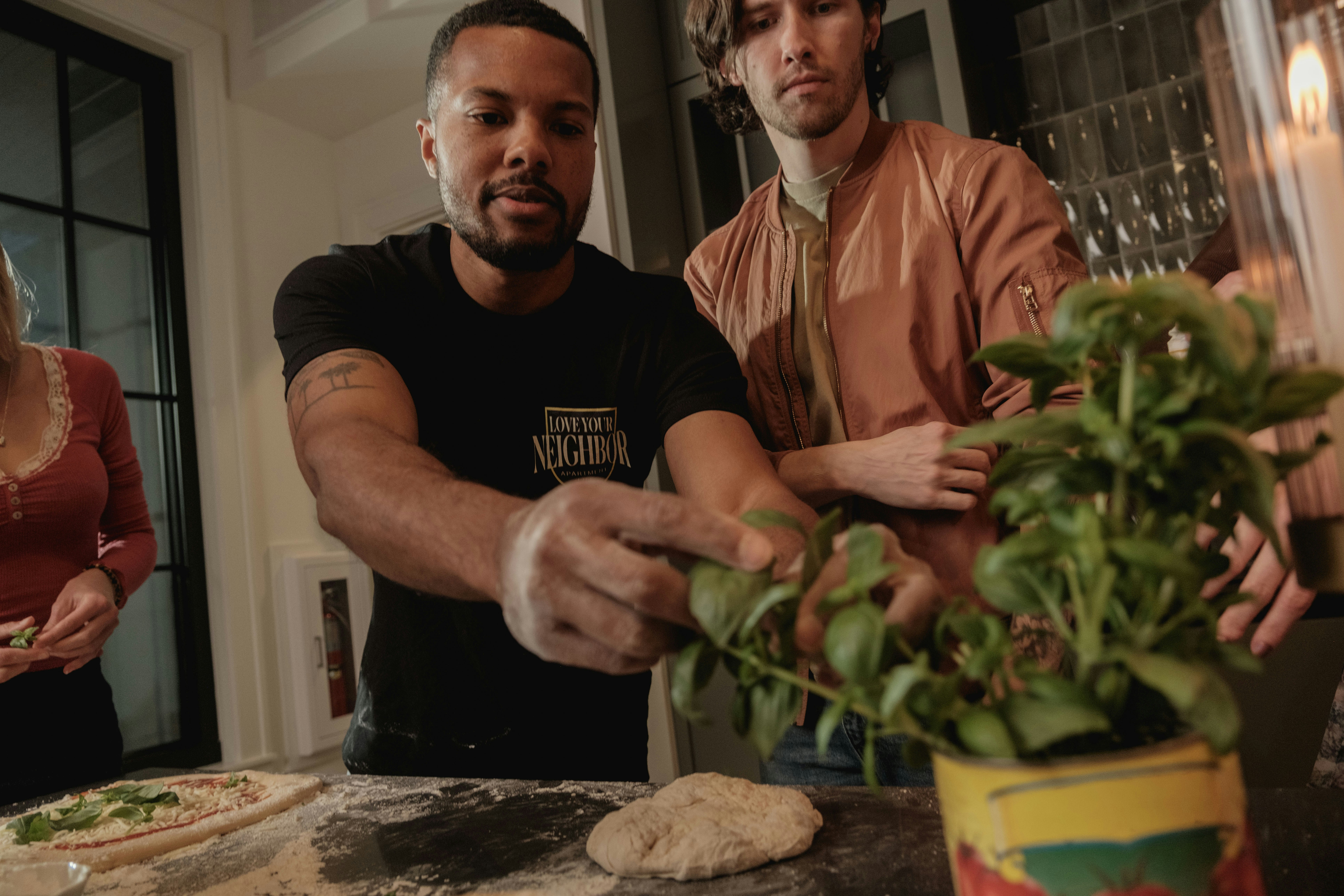 Zwei Männer, die Pizzateig zubereiten und Basilikum hinzufügen.