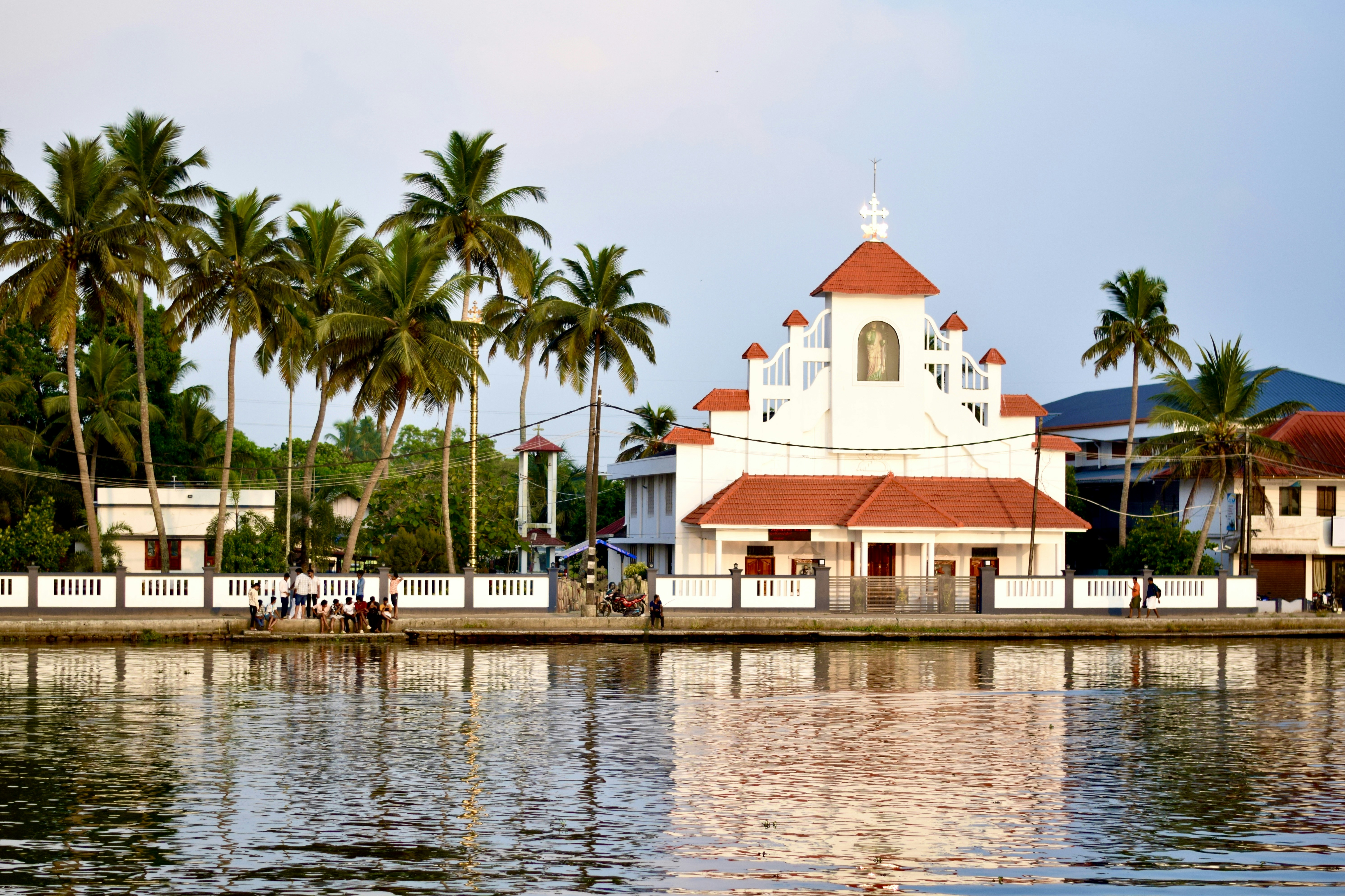 A vibrant photo showing a large church building in Kerala, with a diverse crowd of people including some political figures in the foreground, suggesting a mix of religious and political life.