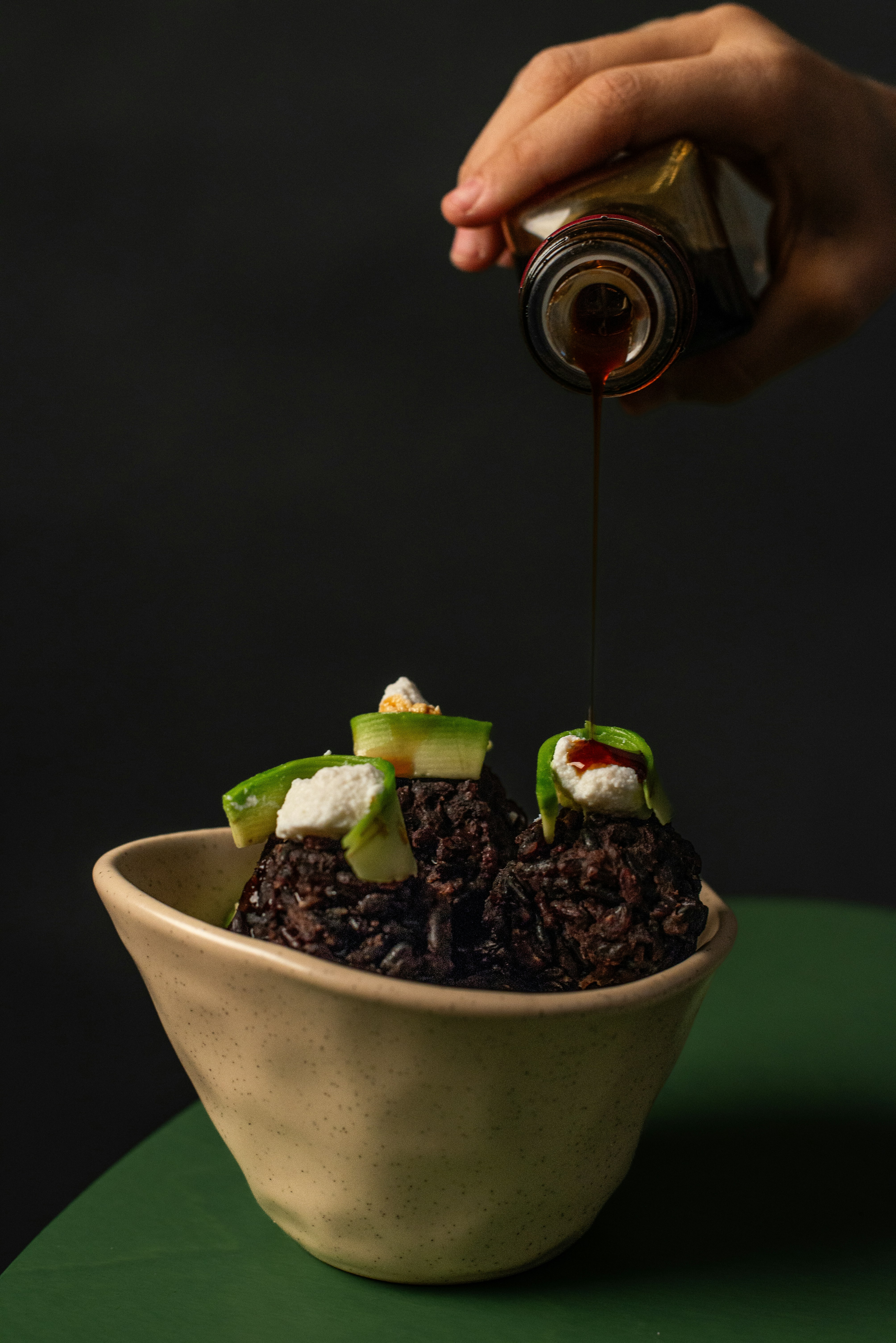 Dark rice dish with avocado and cheese being drizzled