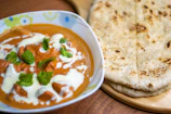 Chicken tikka masala with naan bread on a wooden board.