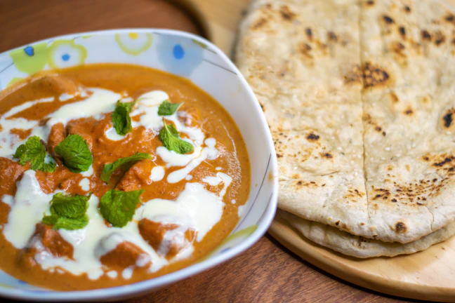 Chicken tikka masala with naan bread on a wooden board.