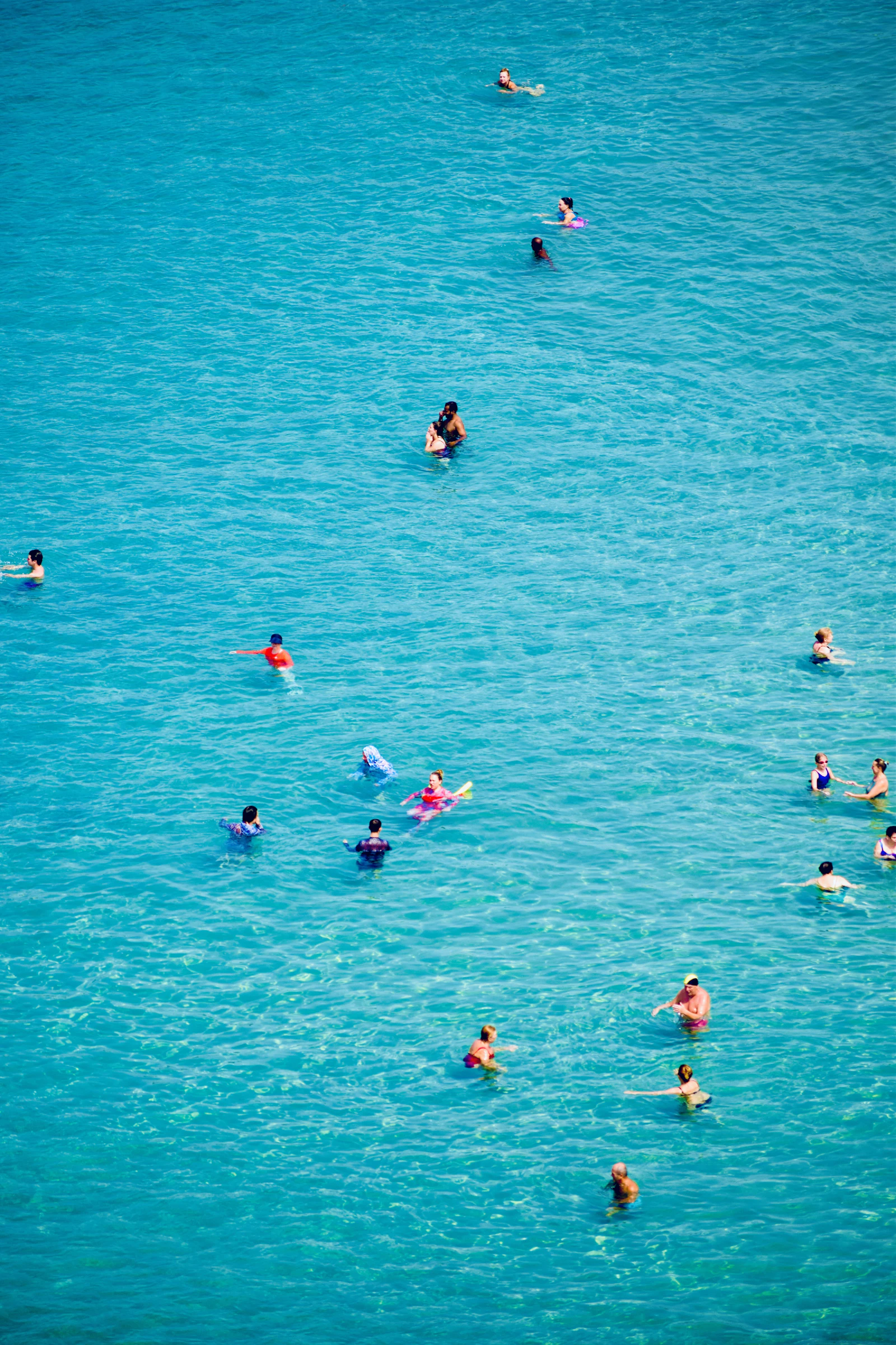 People swimming and relaxing in bright turquoise ocean water at a sandy beach