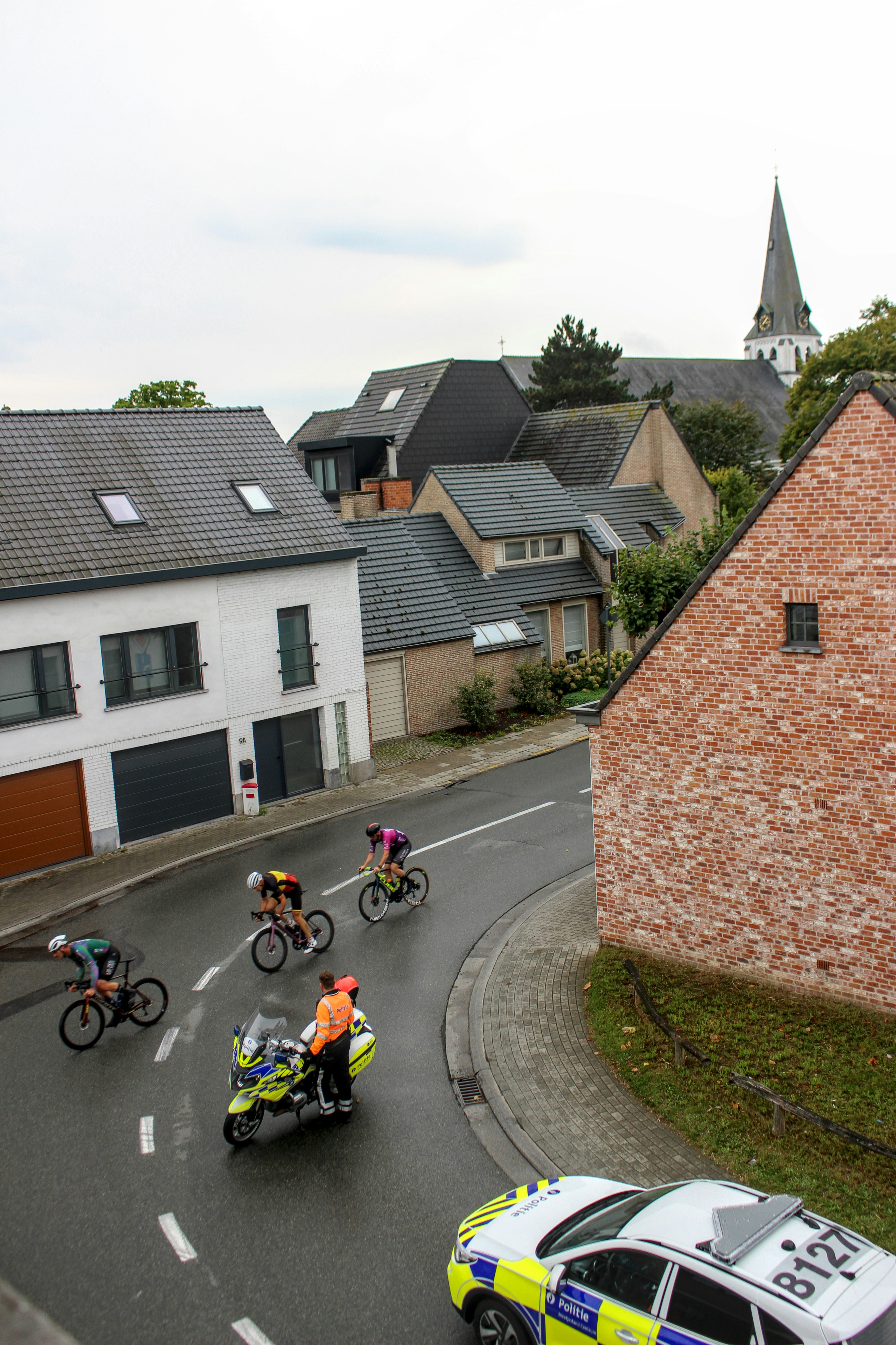 Cyclists race down a street with a police car.