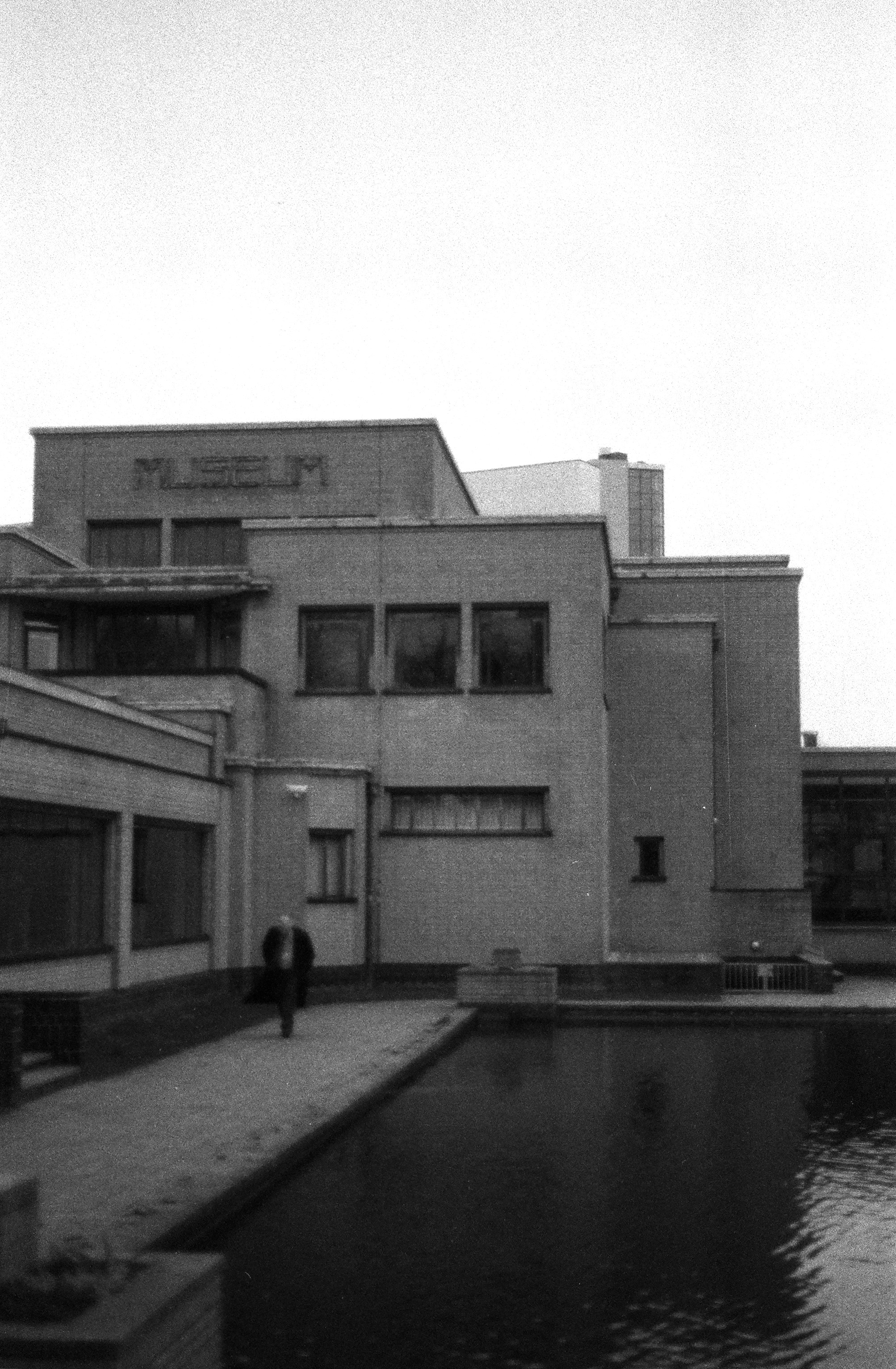 男性が博物館の建物と水のそばを歩いている。