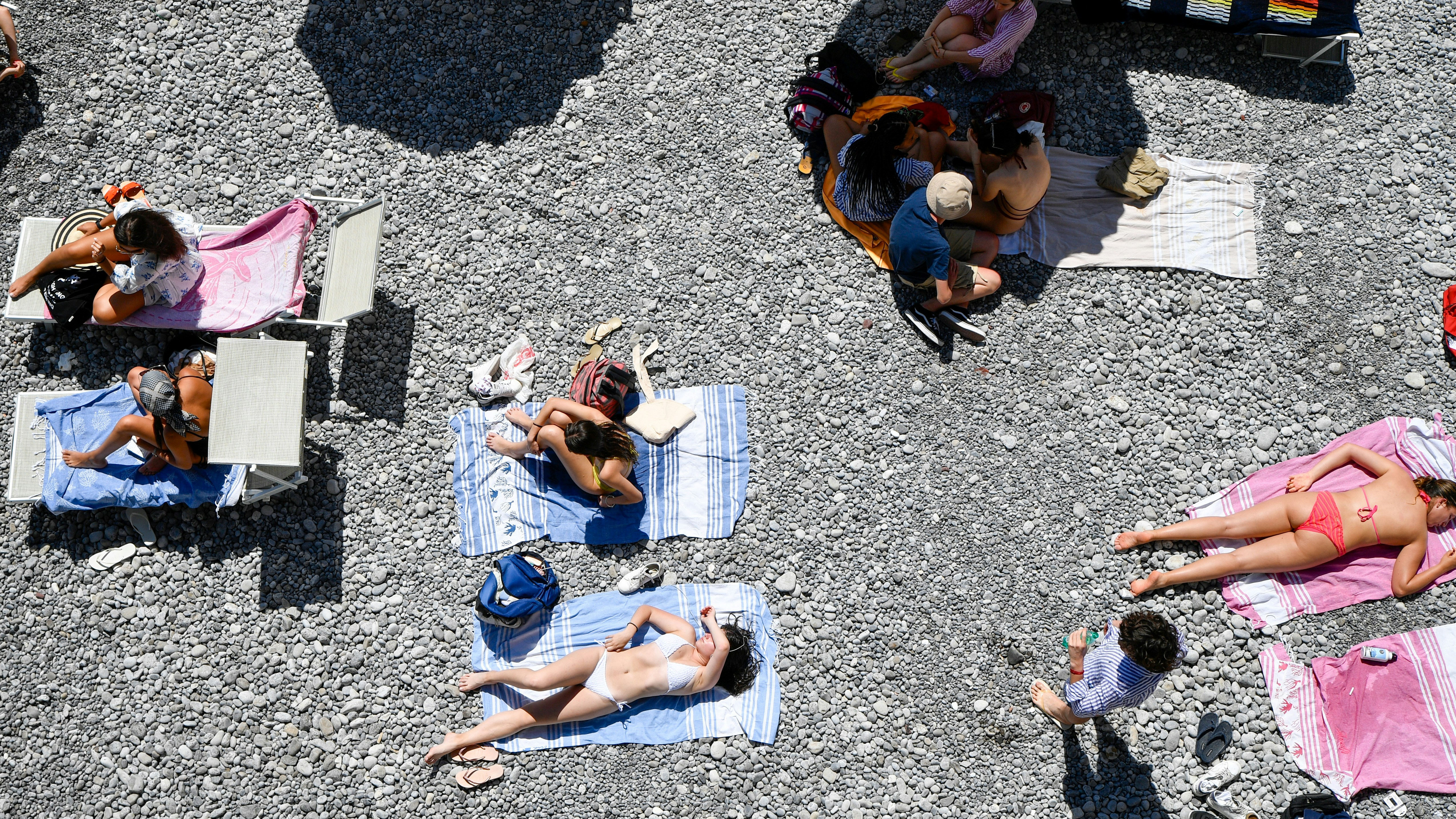 People sunbathing on a rocky beach from above.