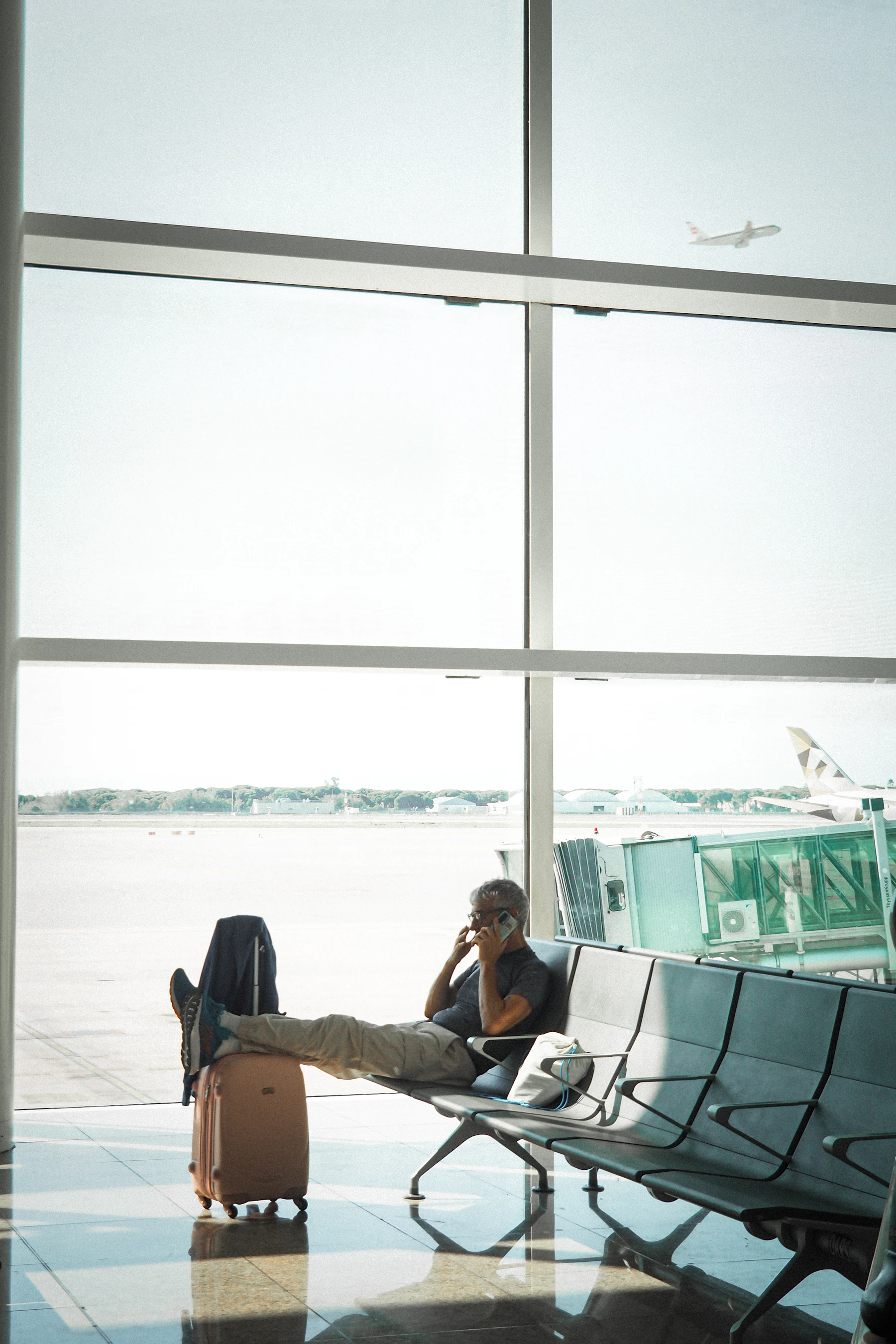 Traveler with rolling luggage using a phone while waiting inside a bright airport terminal