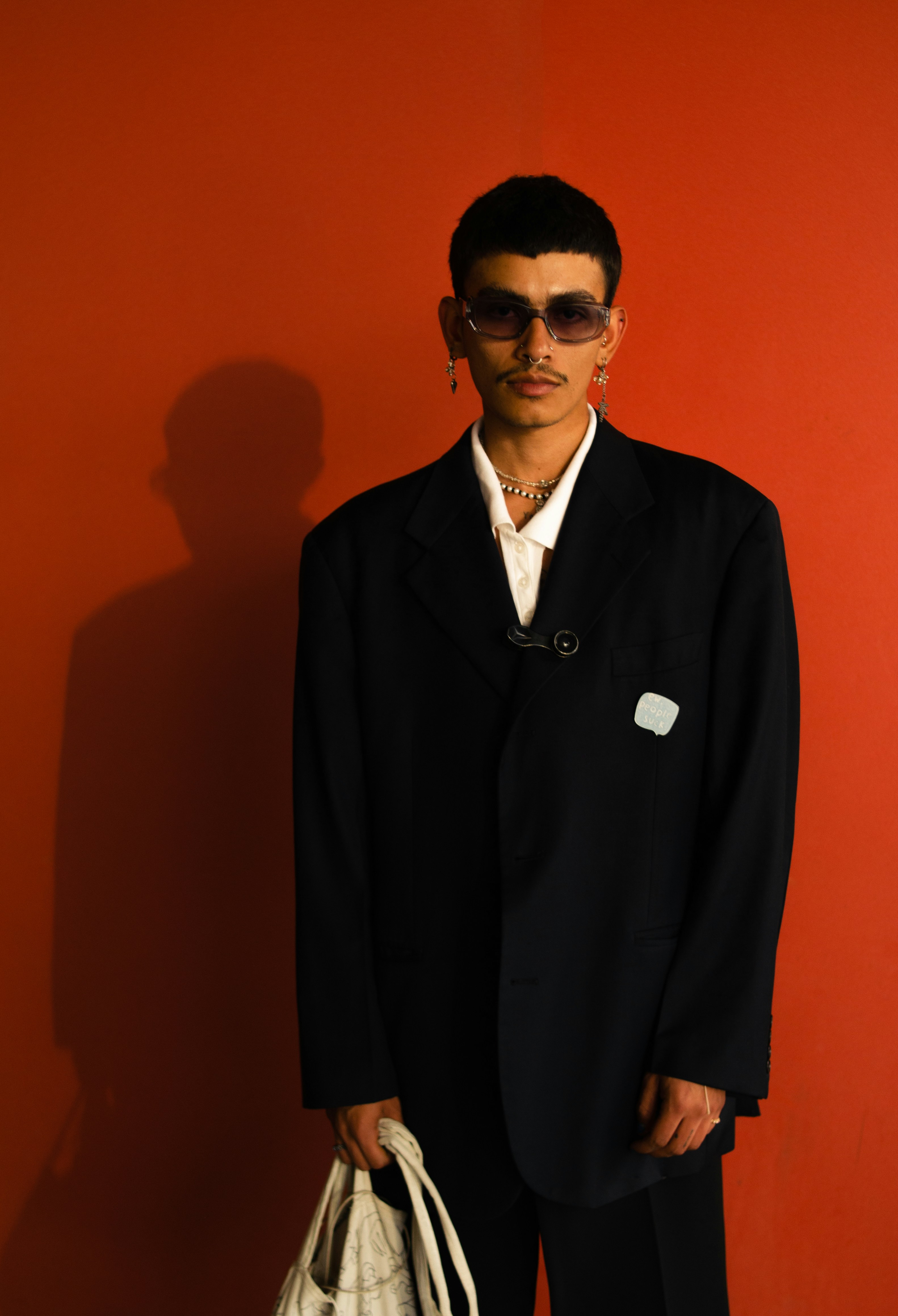 Un hombre con traje negro y gafas de sol sostiene una bolsa.