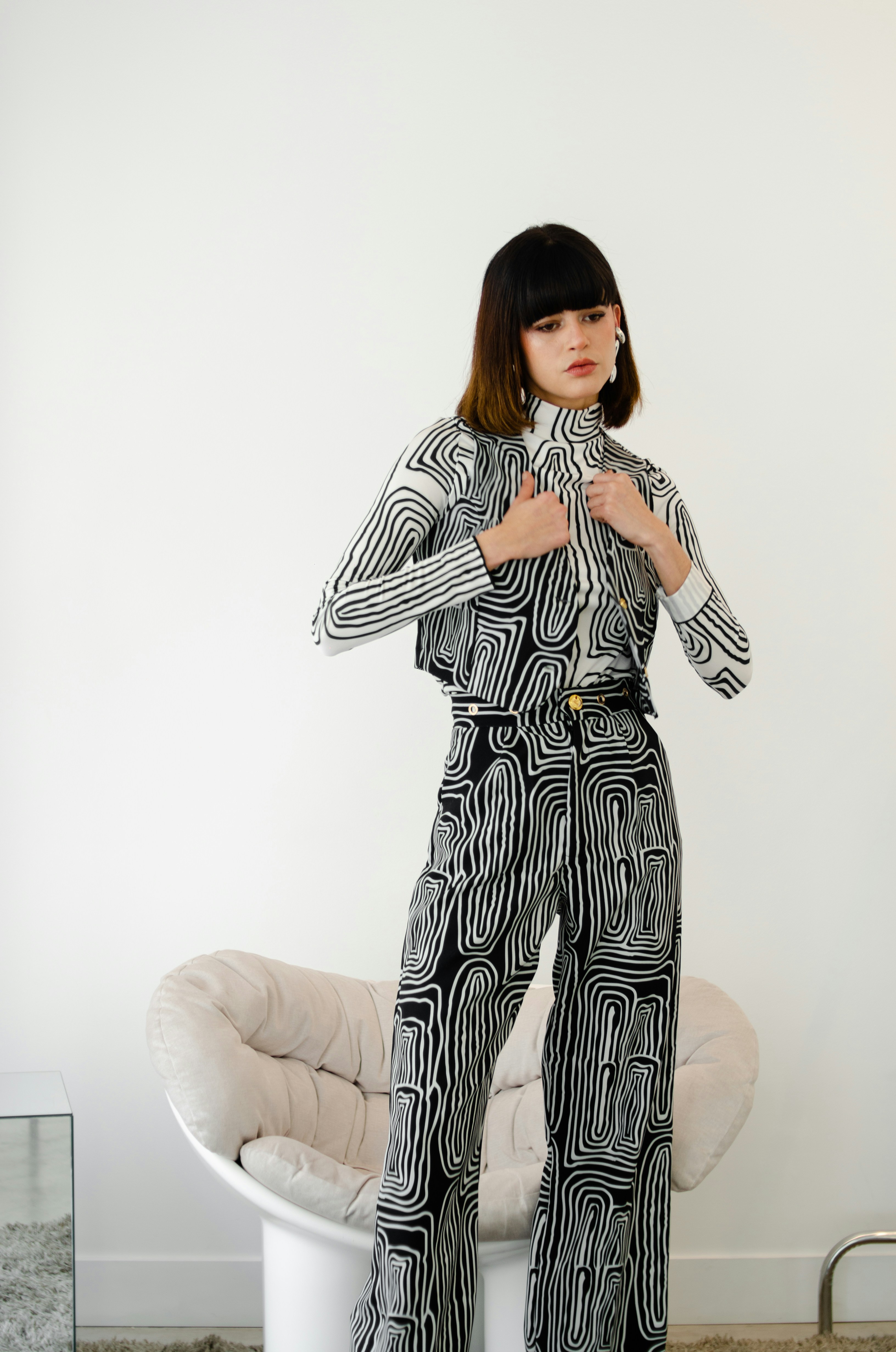 Una mujer con un conjunto abstracto de estampados está de pie cerca de la silla.