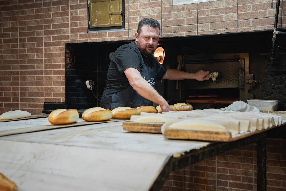 Baker placing fresh bread into a bakery oven