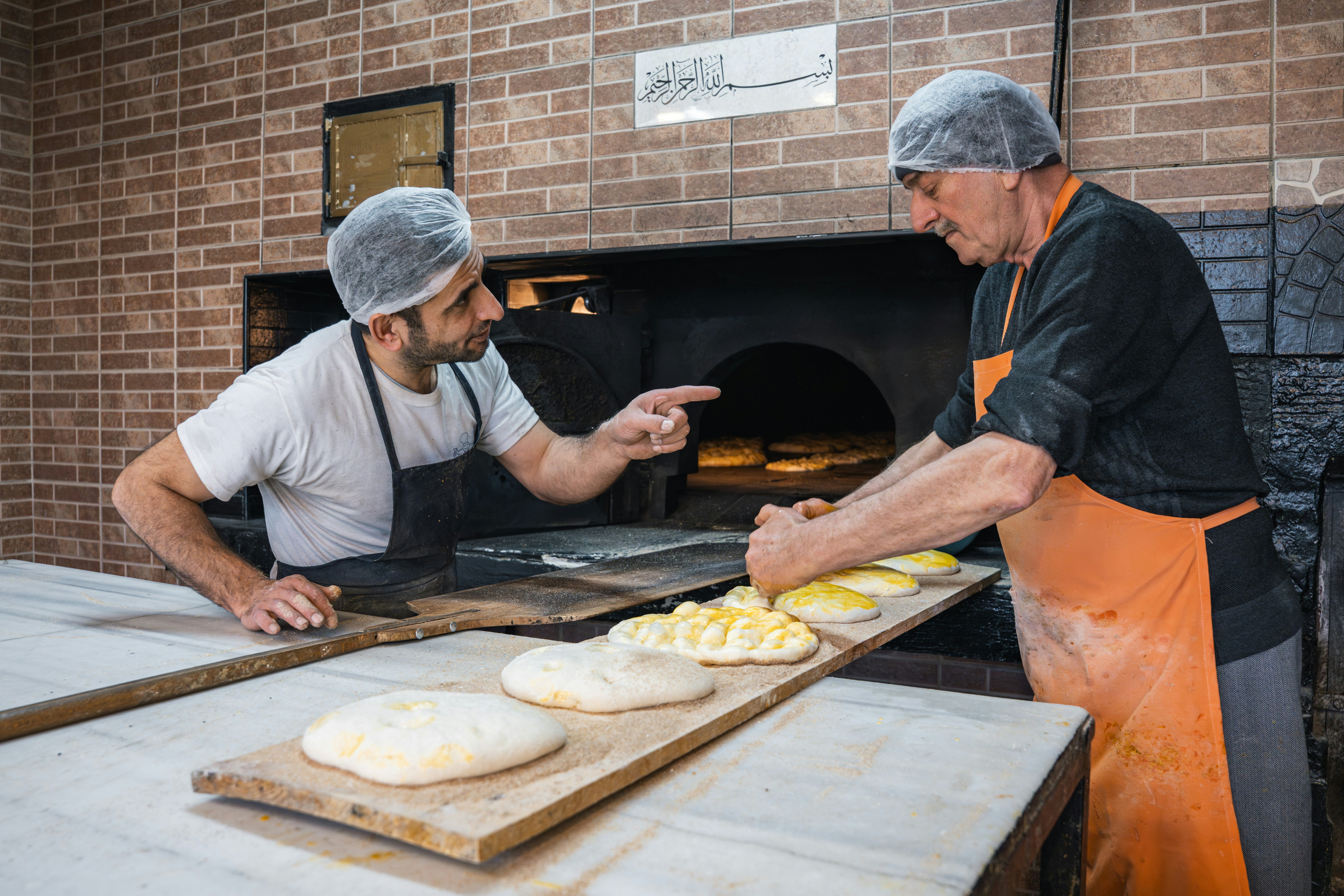 Two bakers preparing dough near a brick oven
