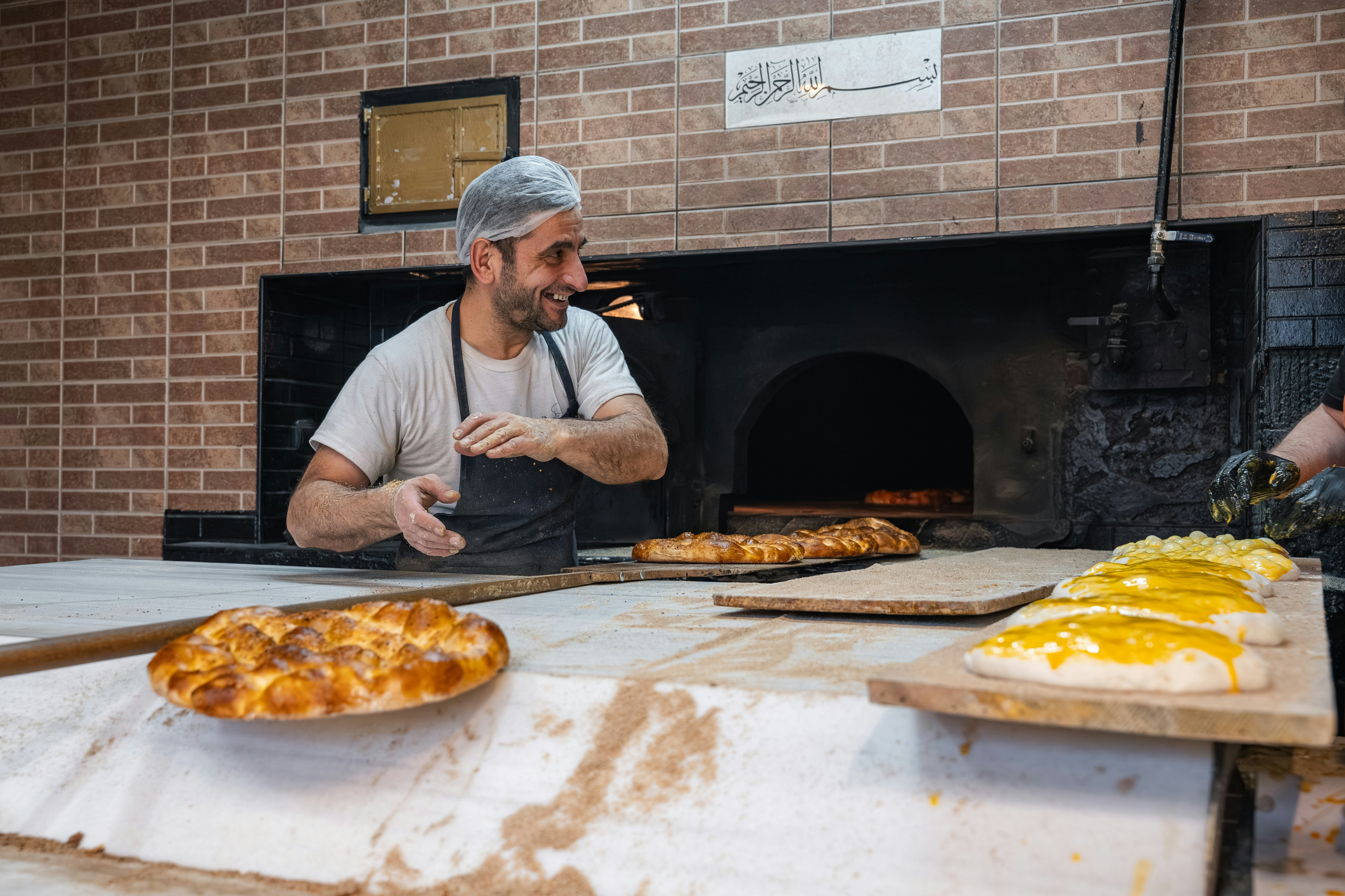 Baker smiling while preparing food in a brick oven.