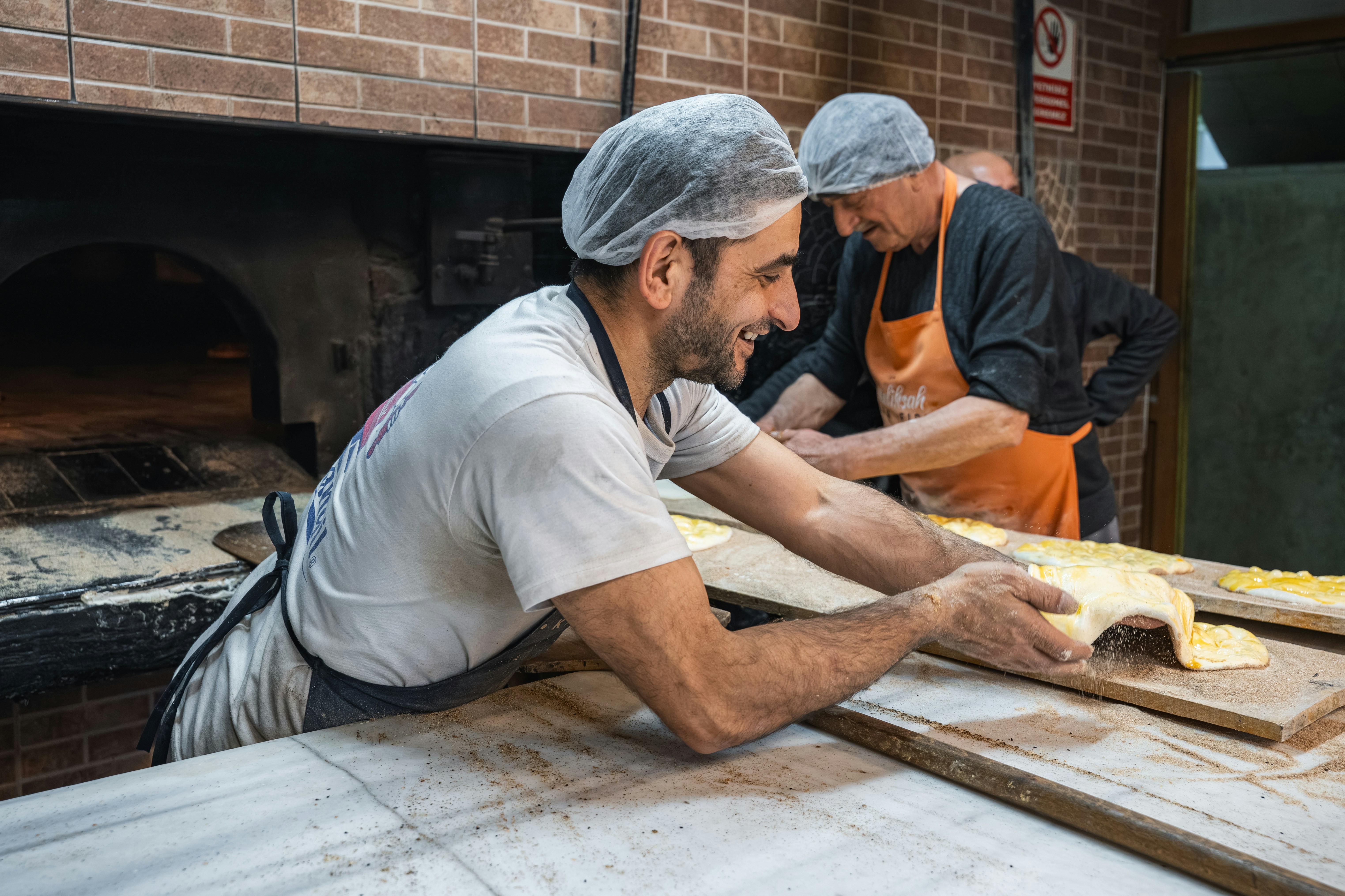 chefs preparing food in a brick oven kitchen smiling and laughing