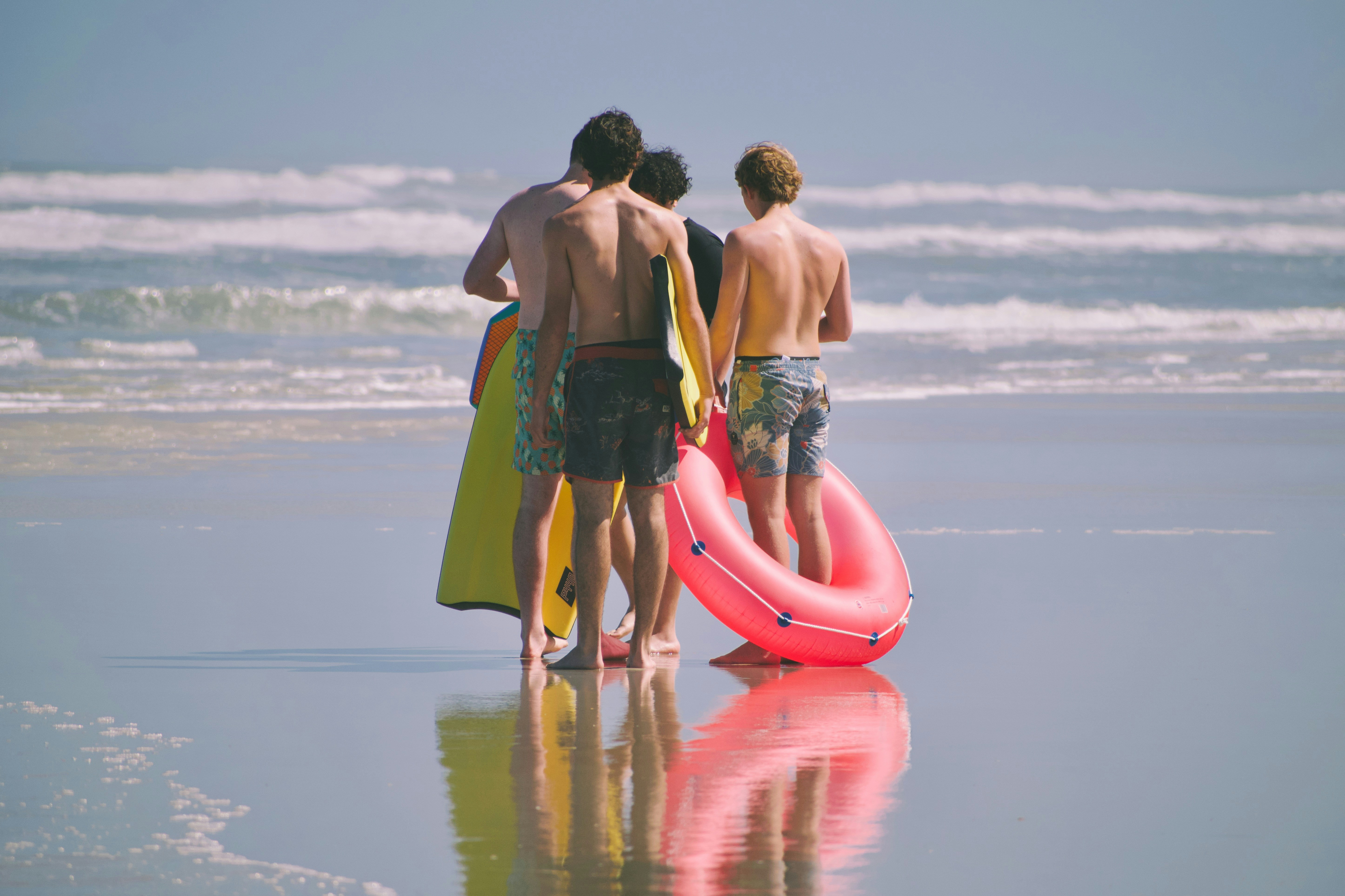 Three people with surfboards and inflatable ring on beach