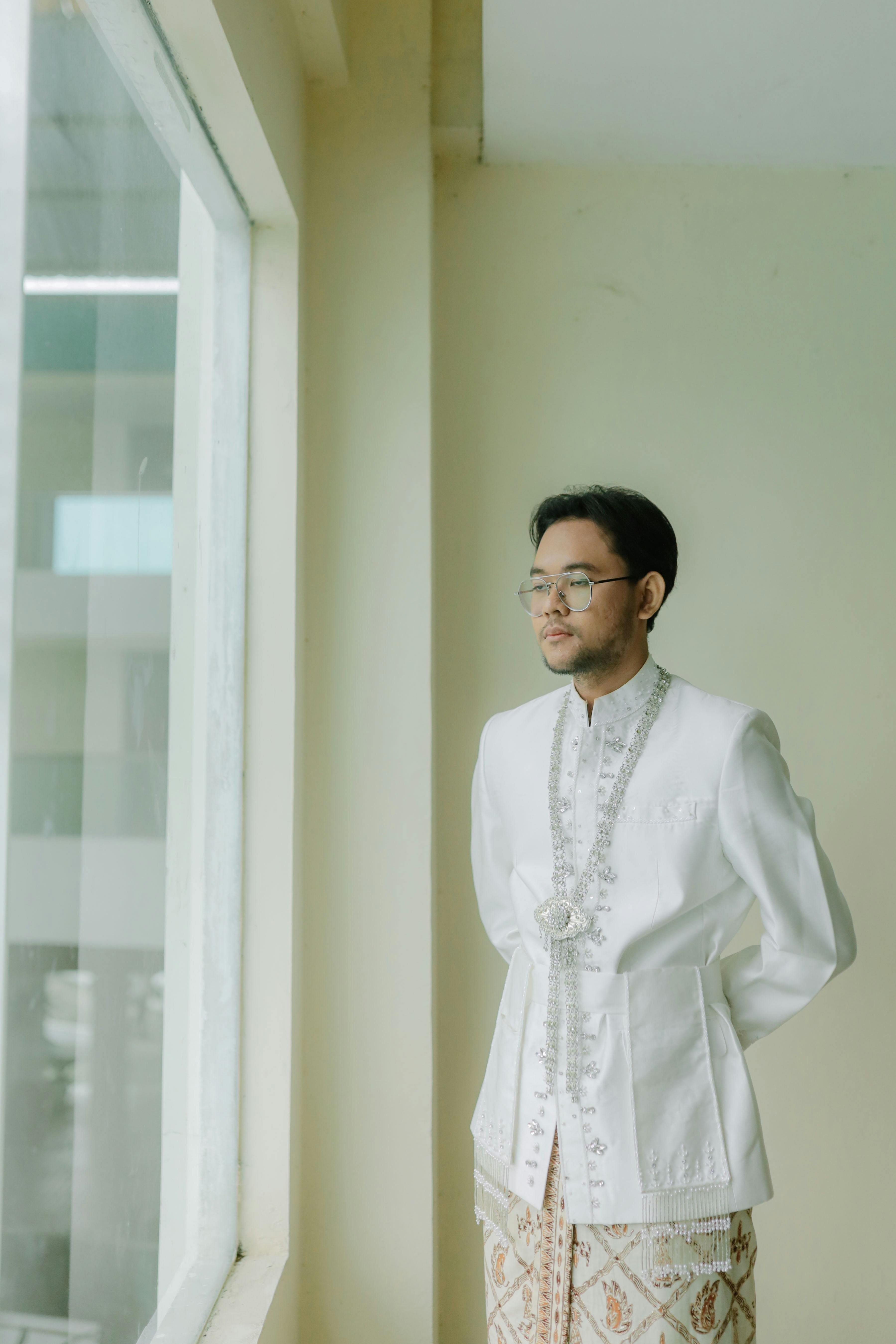 Pria berpakaian putih tradisional di dekat jendela