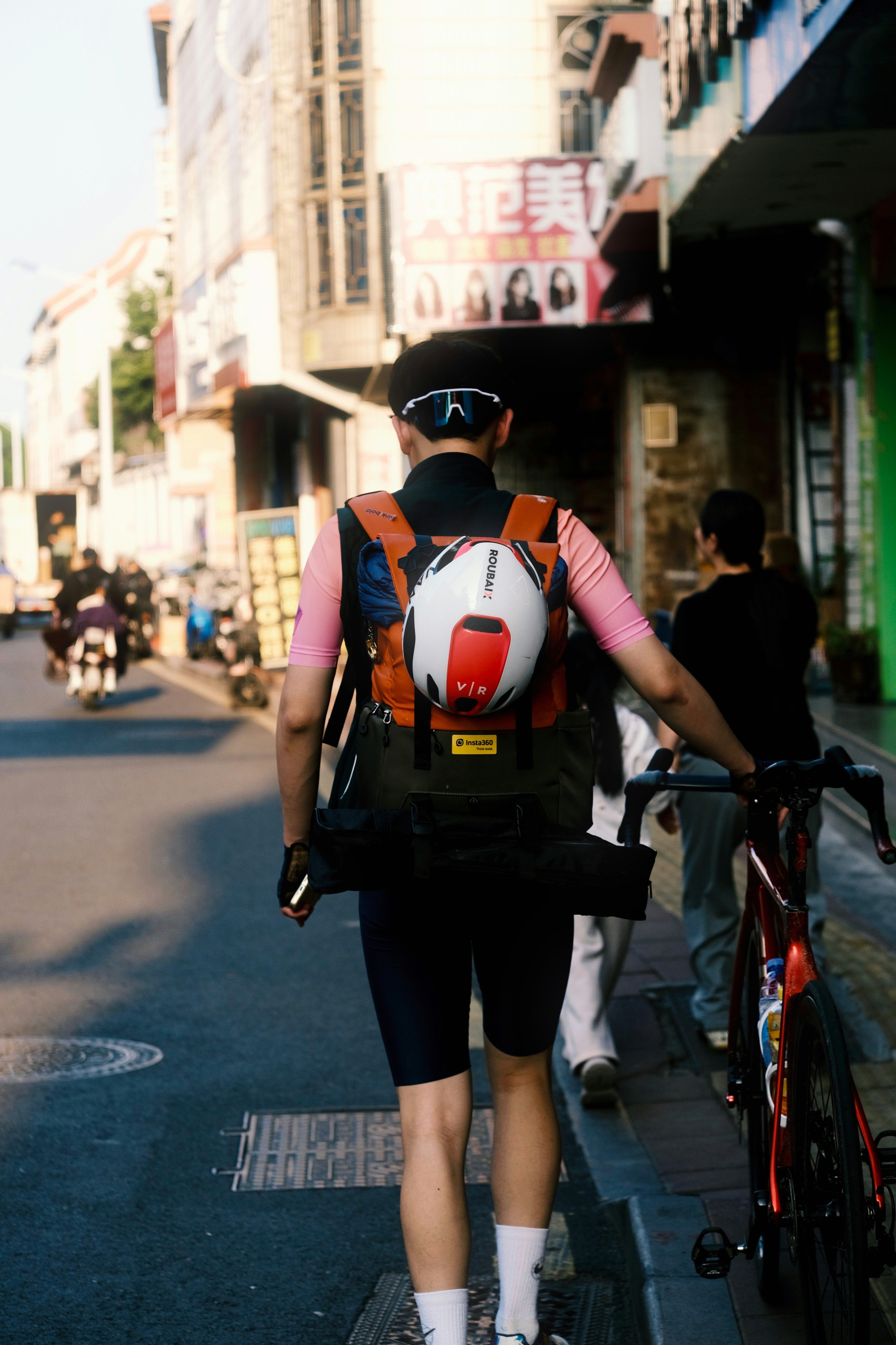 Cyclist with helmet and backpack walks down street.