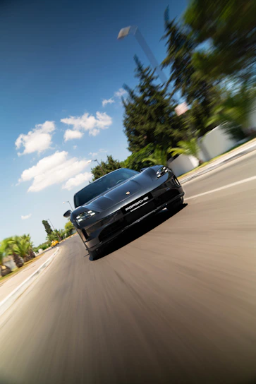 A black sports car driving on a sunny road.