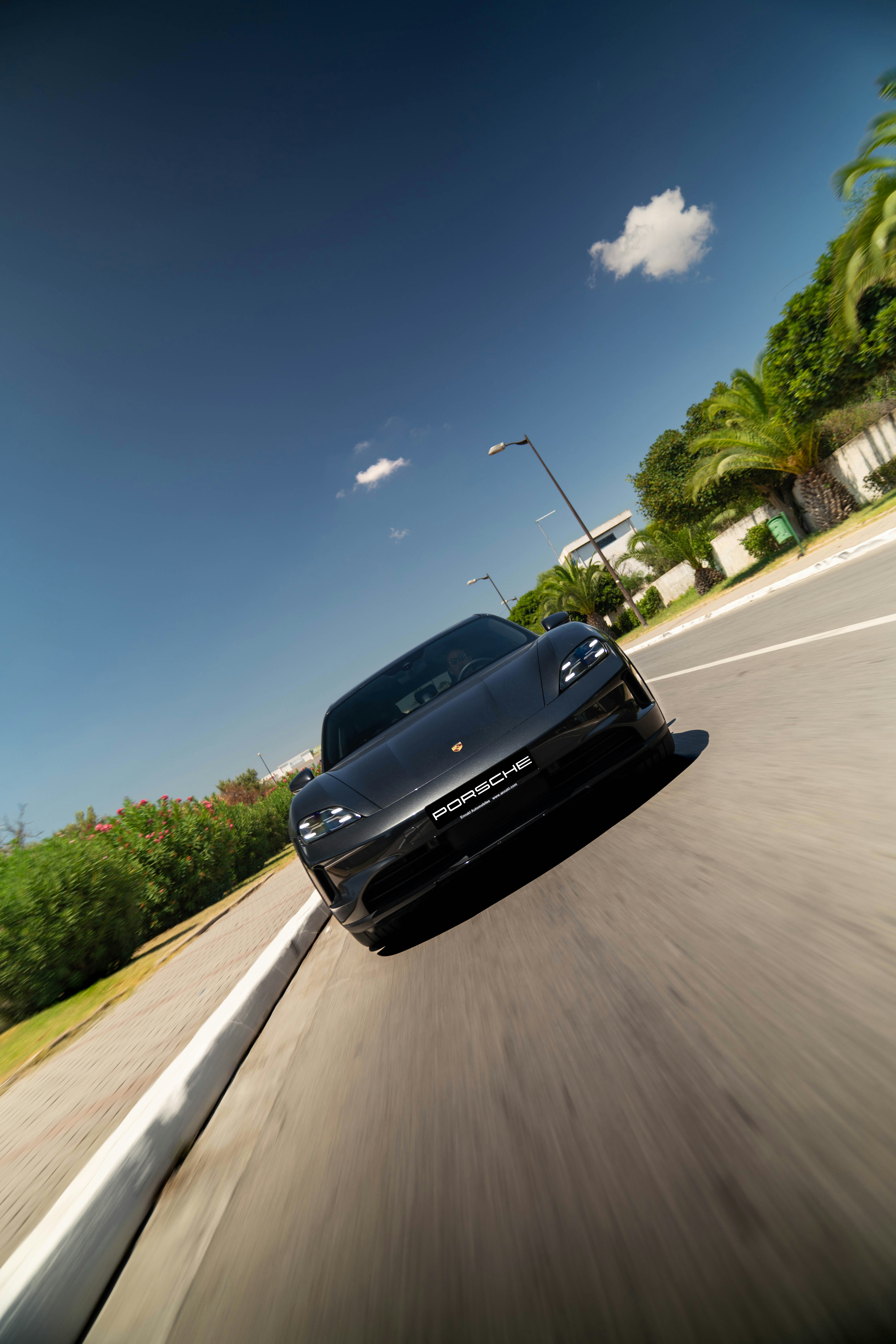 A sleek black porsche drives on a sunny road.