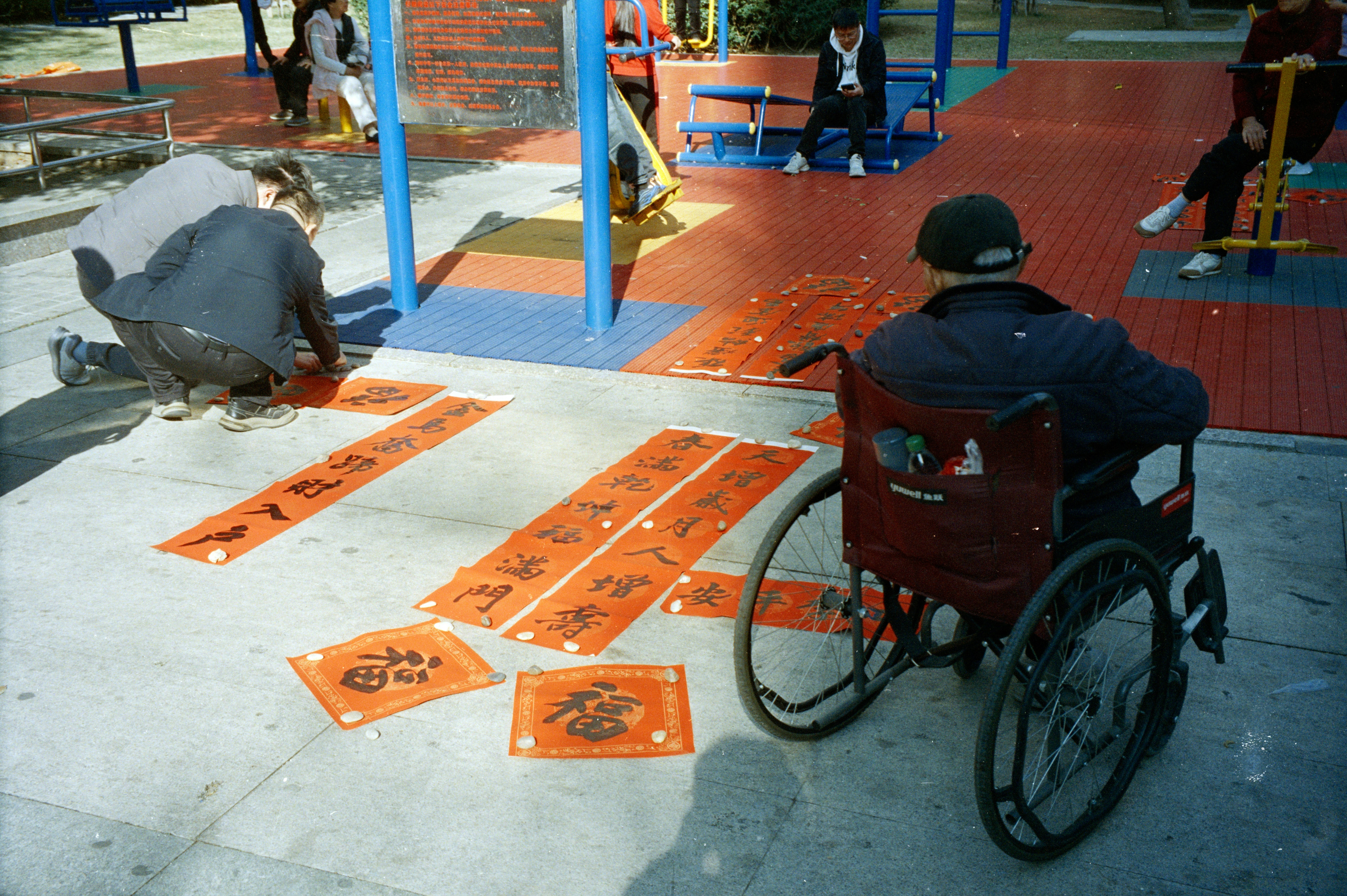 車椅子の男性が書道の巻物を並べる人々を見ている。