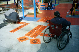 Man in wheelchair watches people arrange calligraphy scrolls.