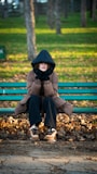 A person bundled up on a park bench in autumn.