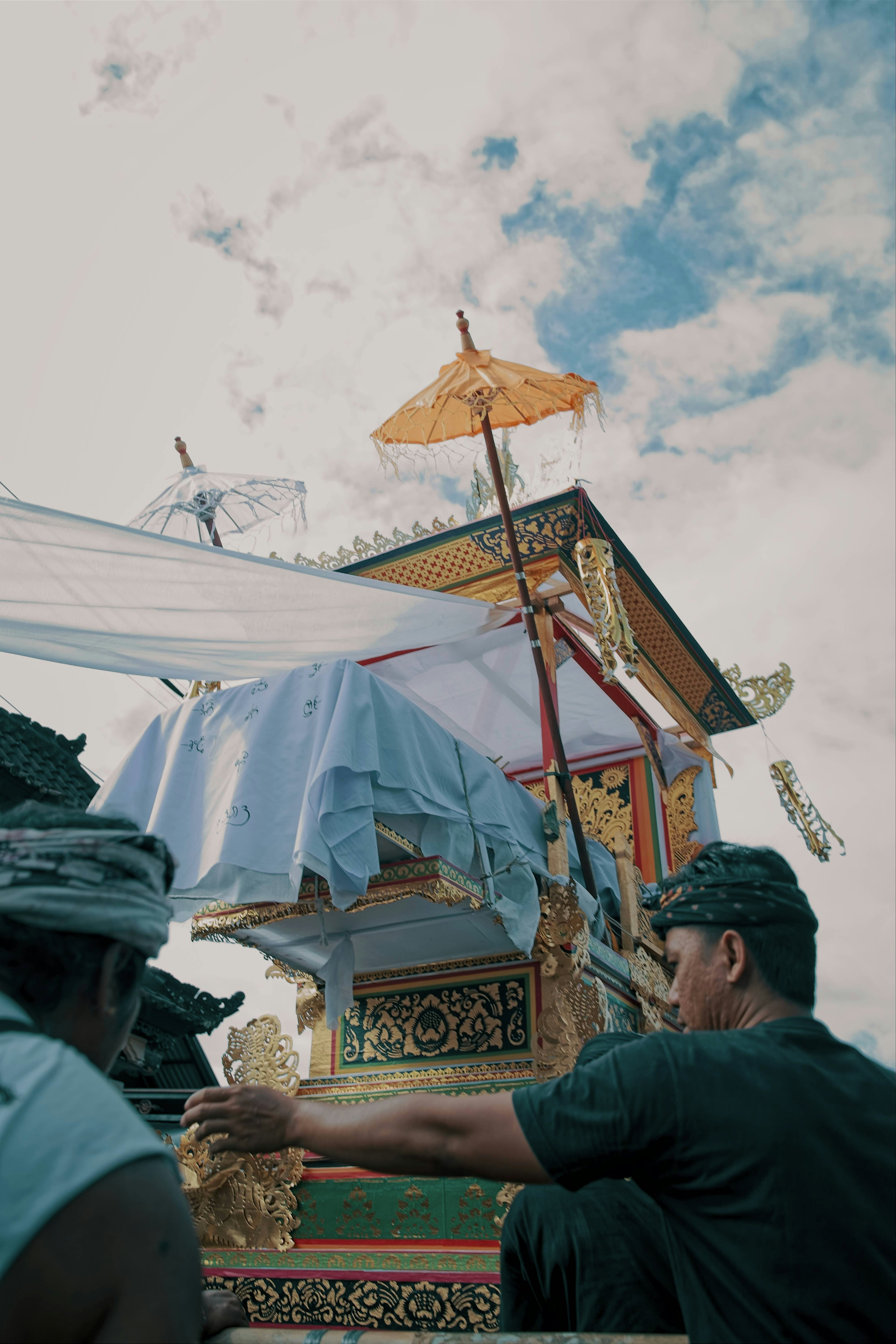 People prepare ornate ceremonial float under cloudy sky