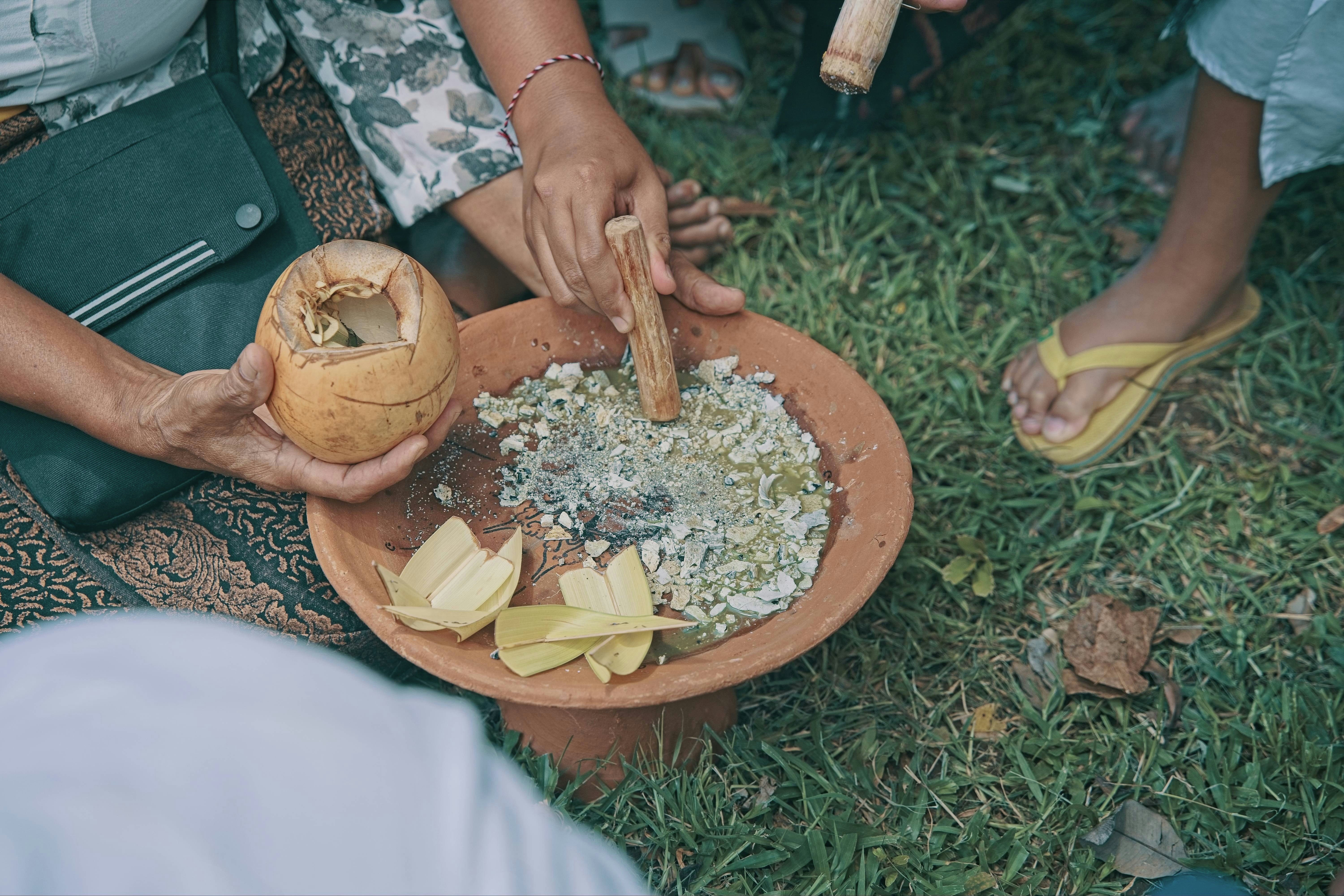 Hands preparing food in a clay bowl outdoors.