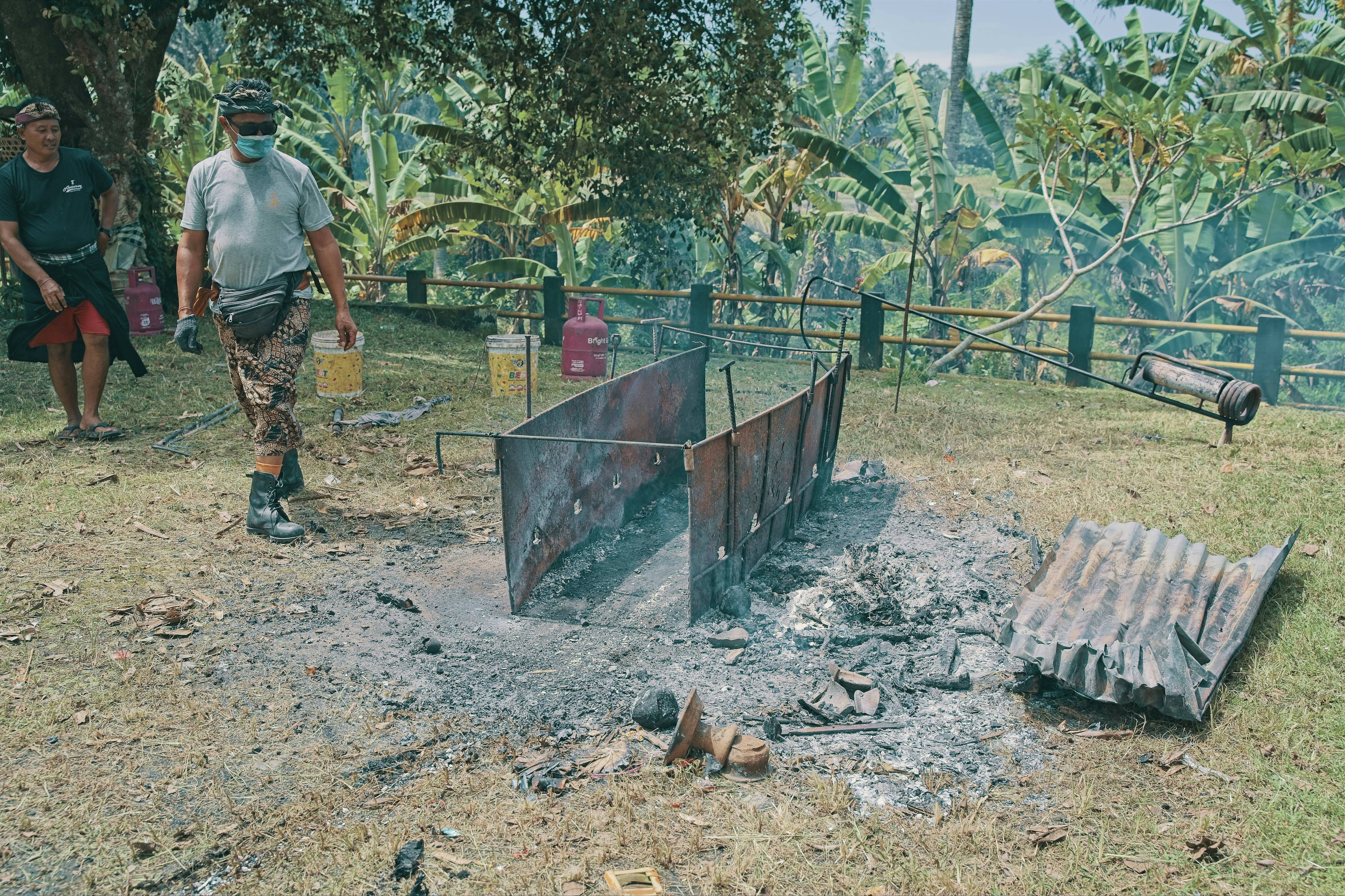 Men preparing a barbecue pit with firewood and cooking equipment