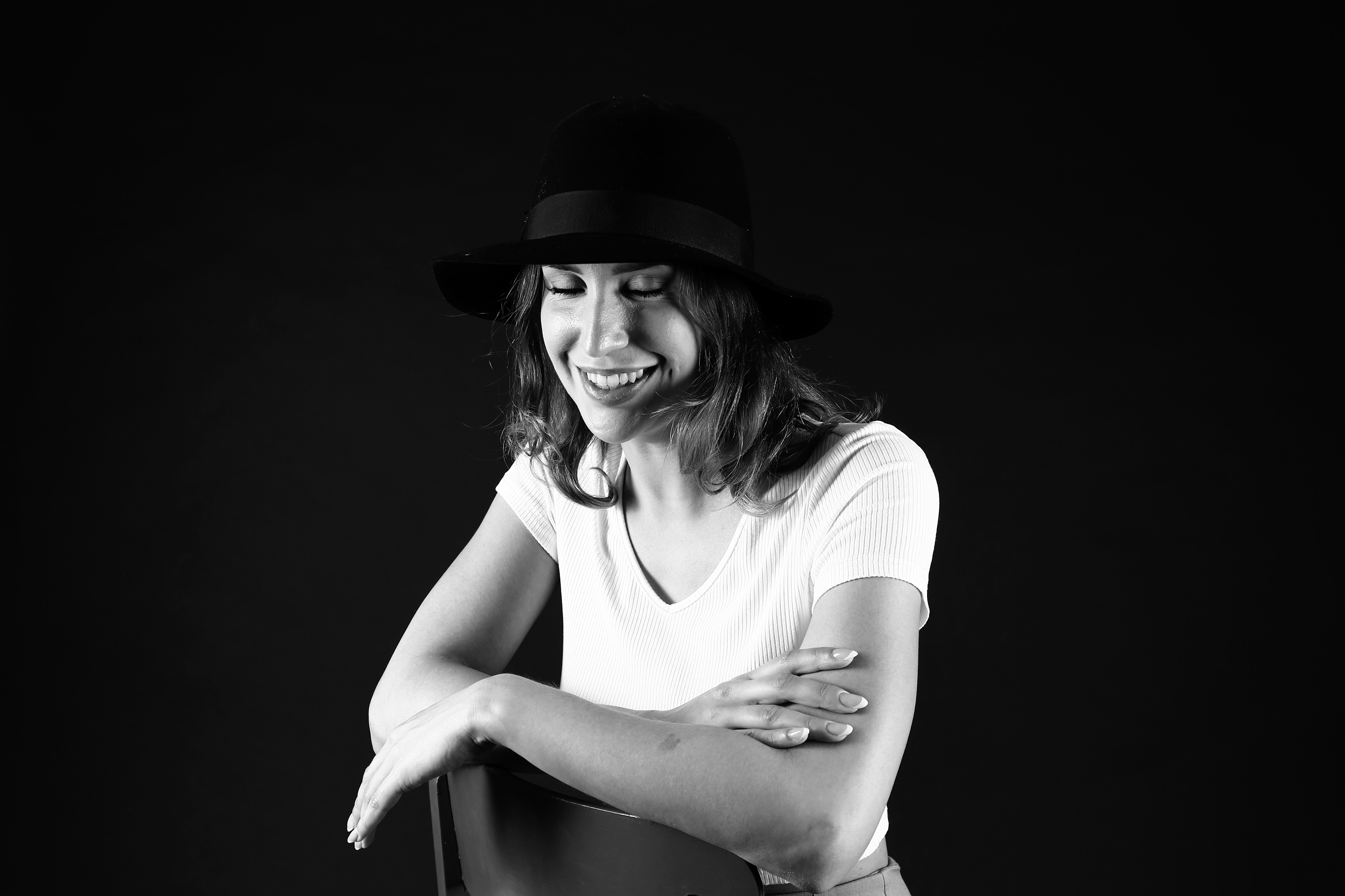 黒い帽子をかぶった女性が暗い背景に微笑む