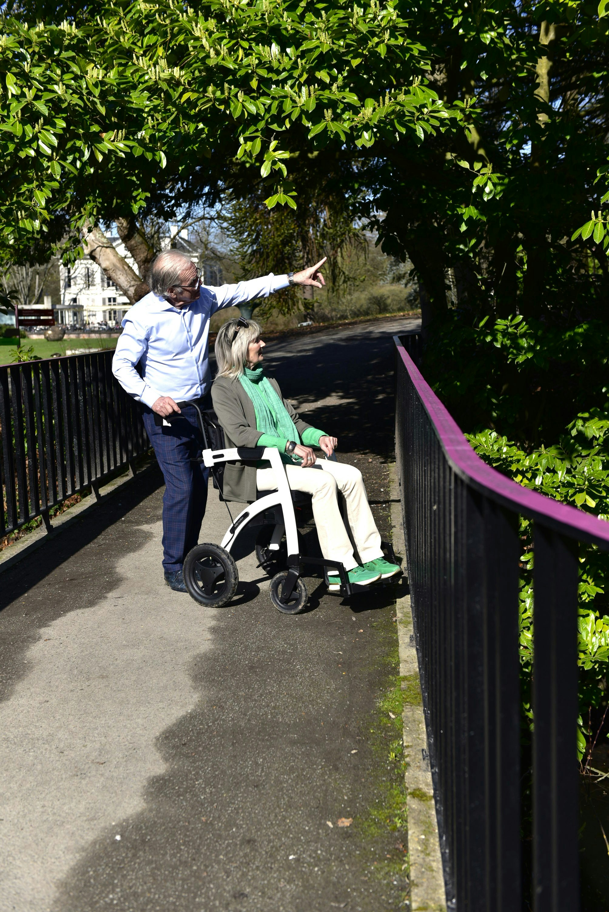 Man and woman on a walkway, pointing at trees.