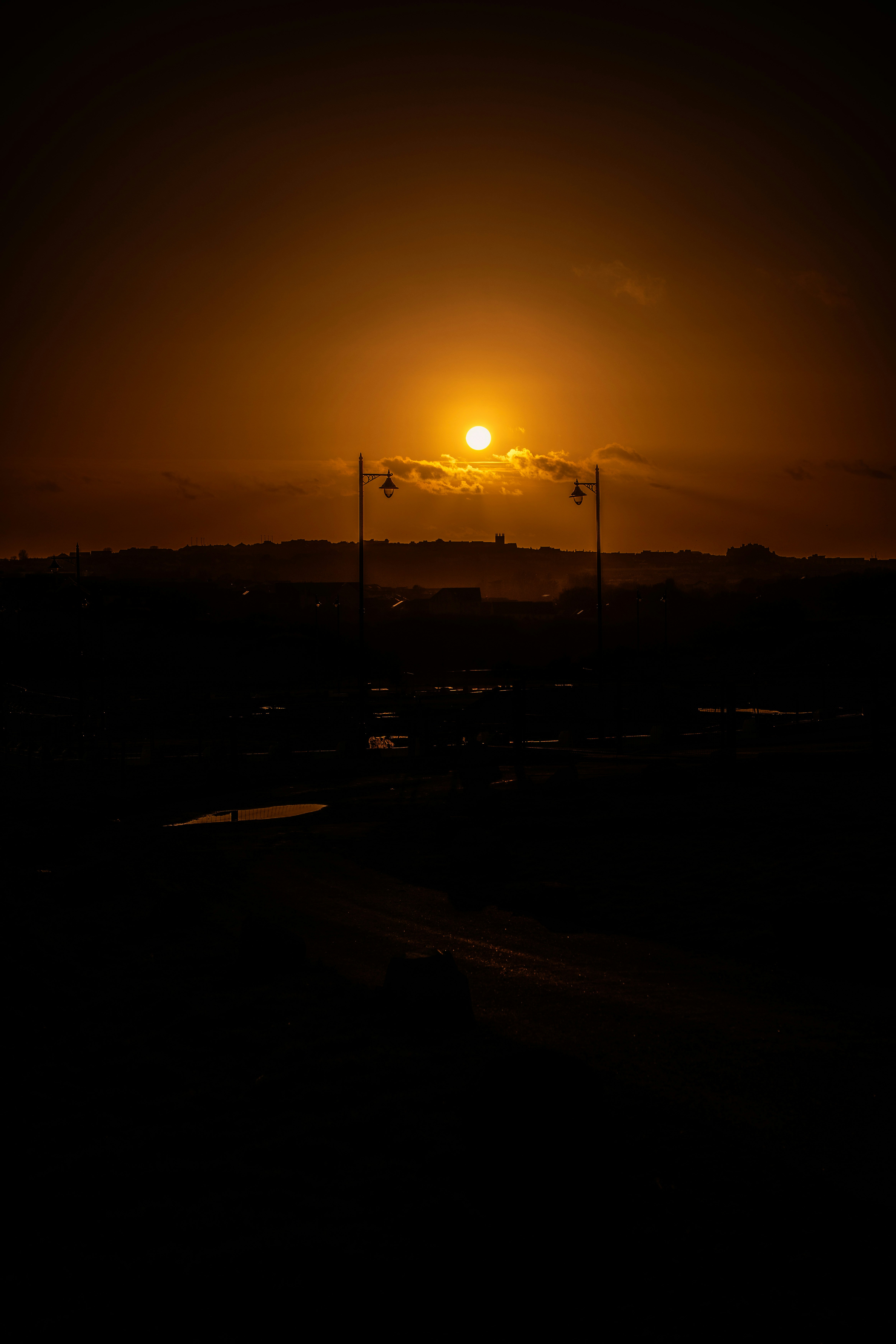 The sun sets over a dark, silhouetted landscape.